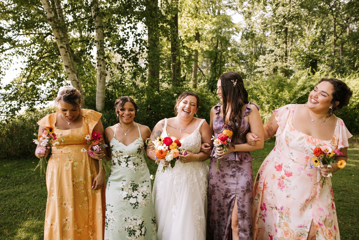 A group in colorful floral and pastel dresses poses together in a garden setting during a special occasion.