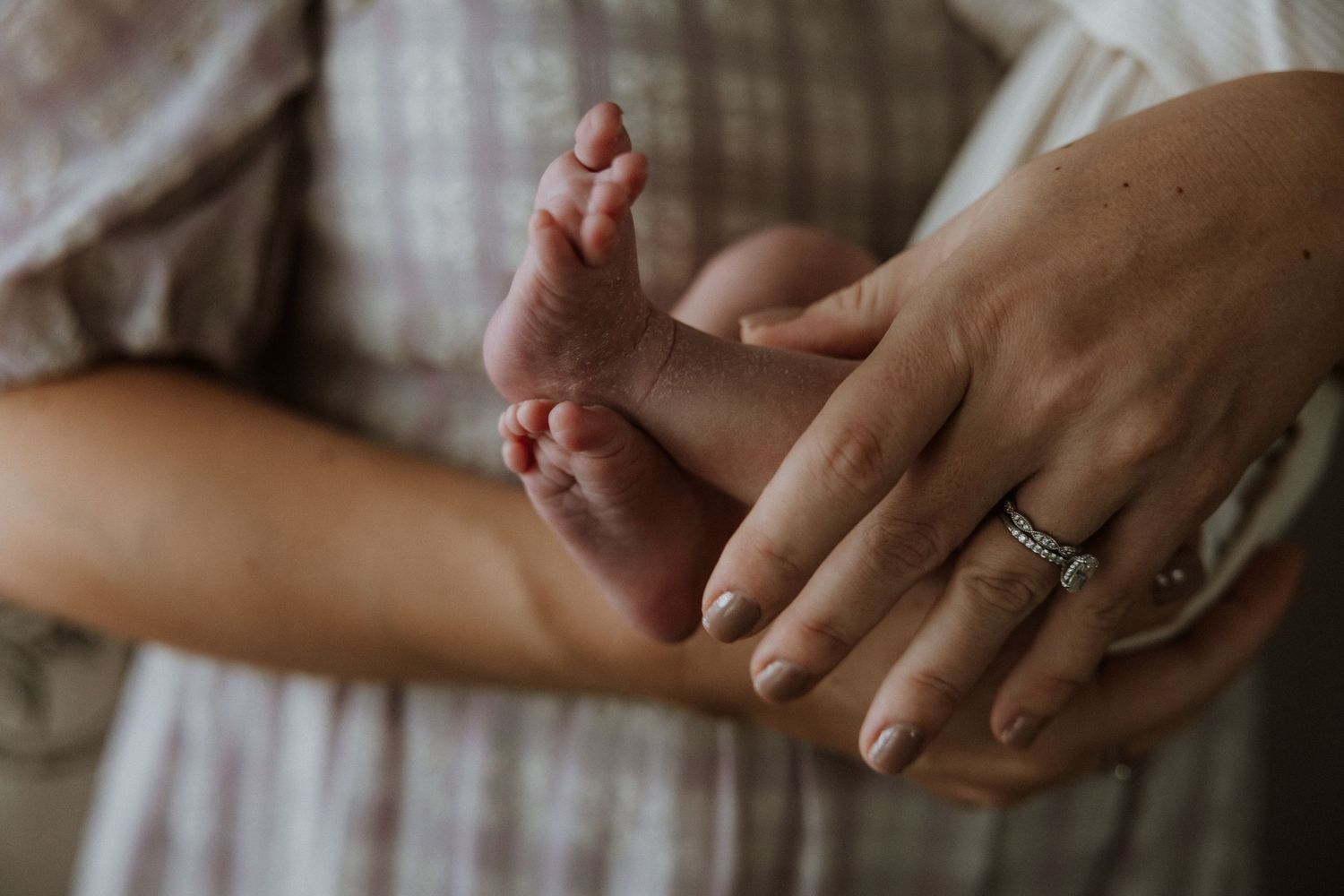 Close-up of tiny baby feet being gently held by hands with a wedding ring.