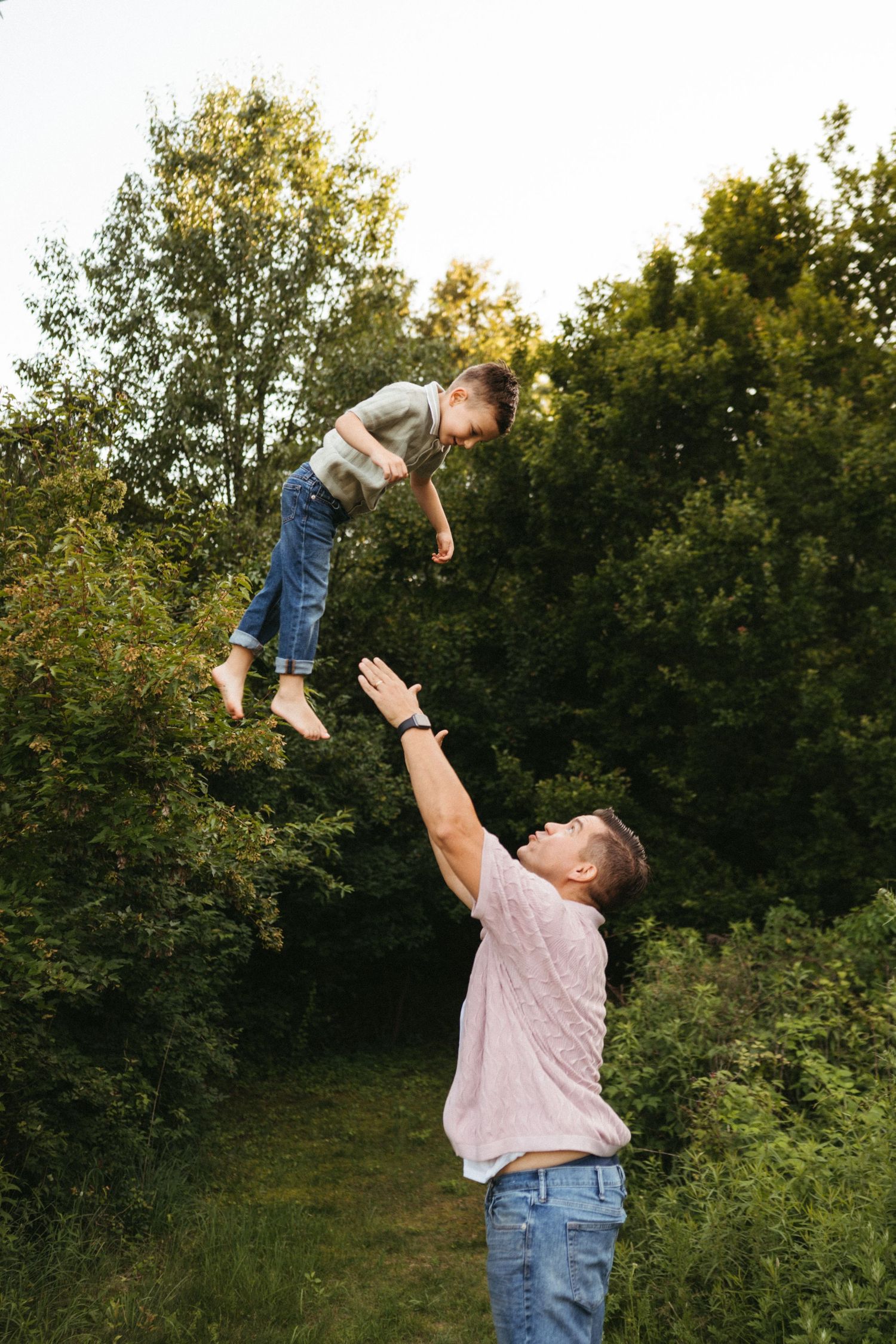 A playful outdoor scene where a person tosses a child high into the air on a sunny summer day.