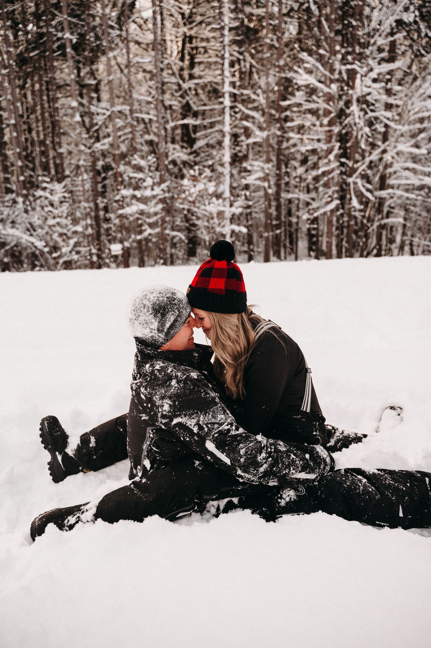 Intimate winter moment between couple in snow with forest backdrop.