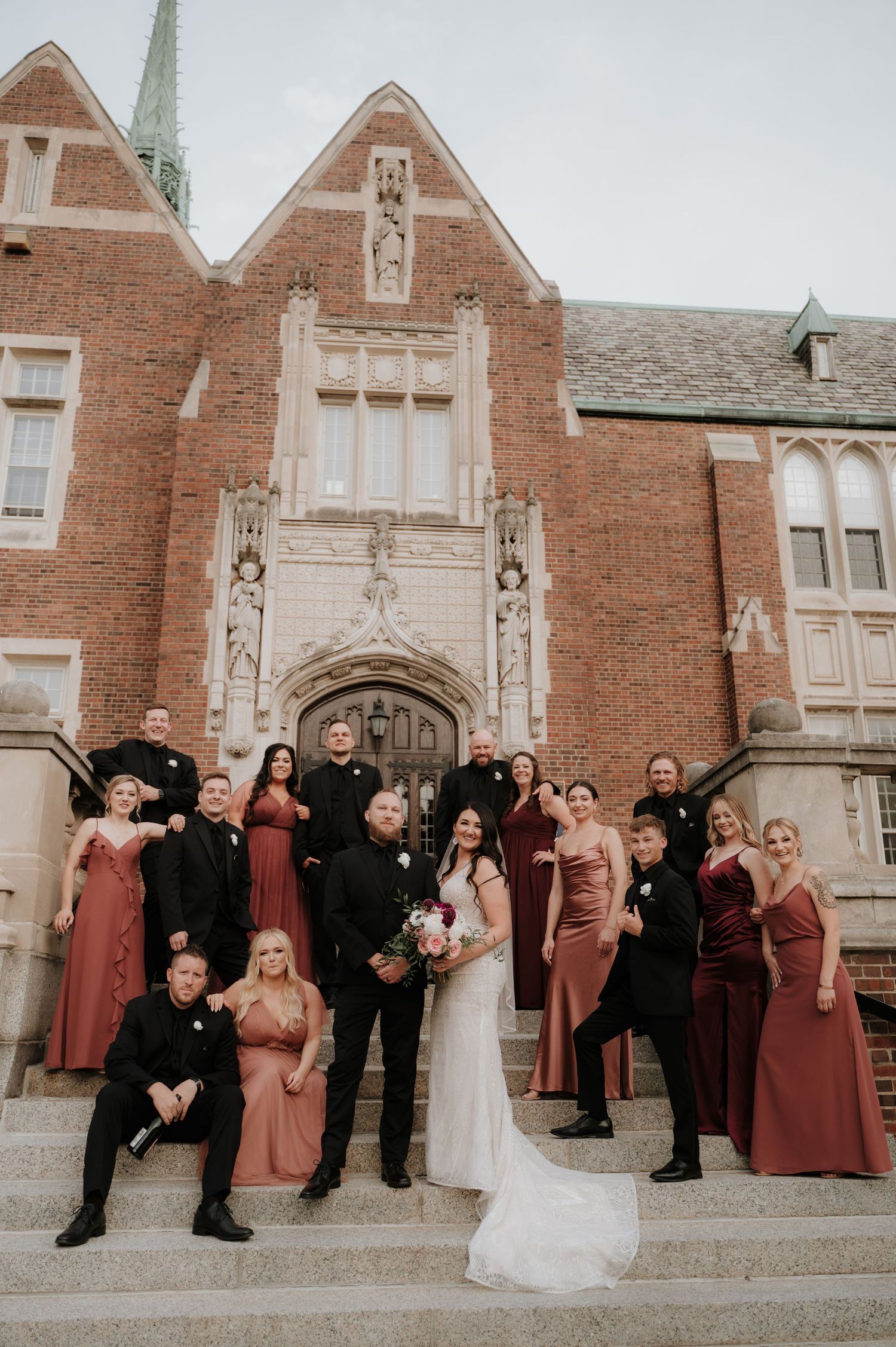 Fun group photo of wedding party posing playfully outside historic brick church.