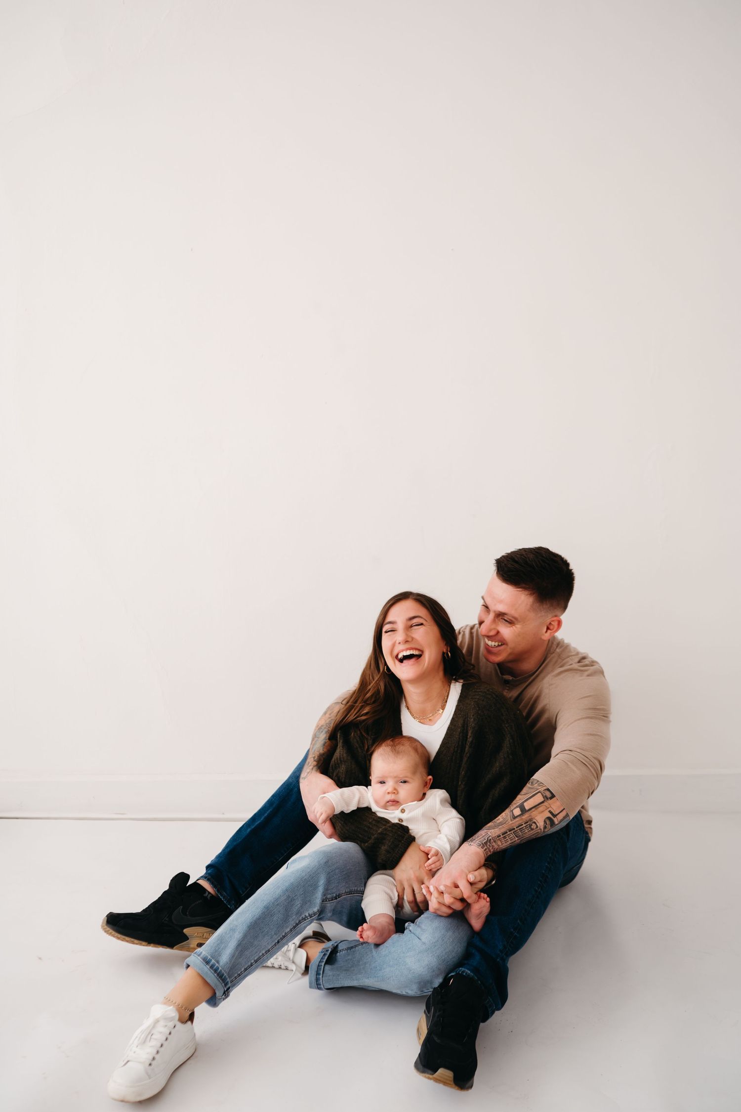 Family of three sits on floor sharing joyful laughter during casual photo session.