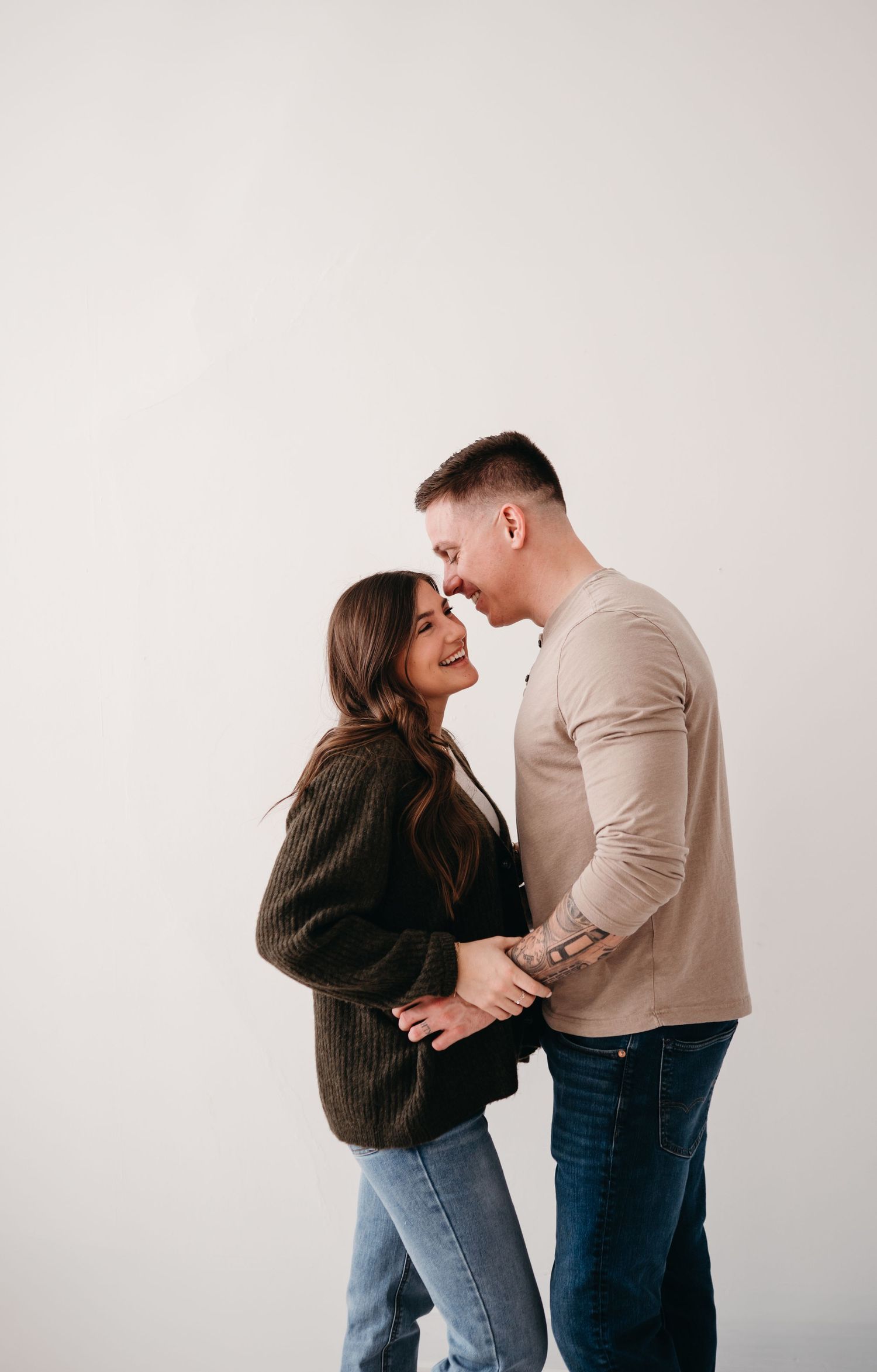 A couple in casual clothes shares an intimate moment against a white background.