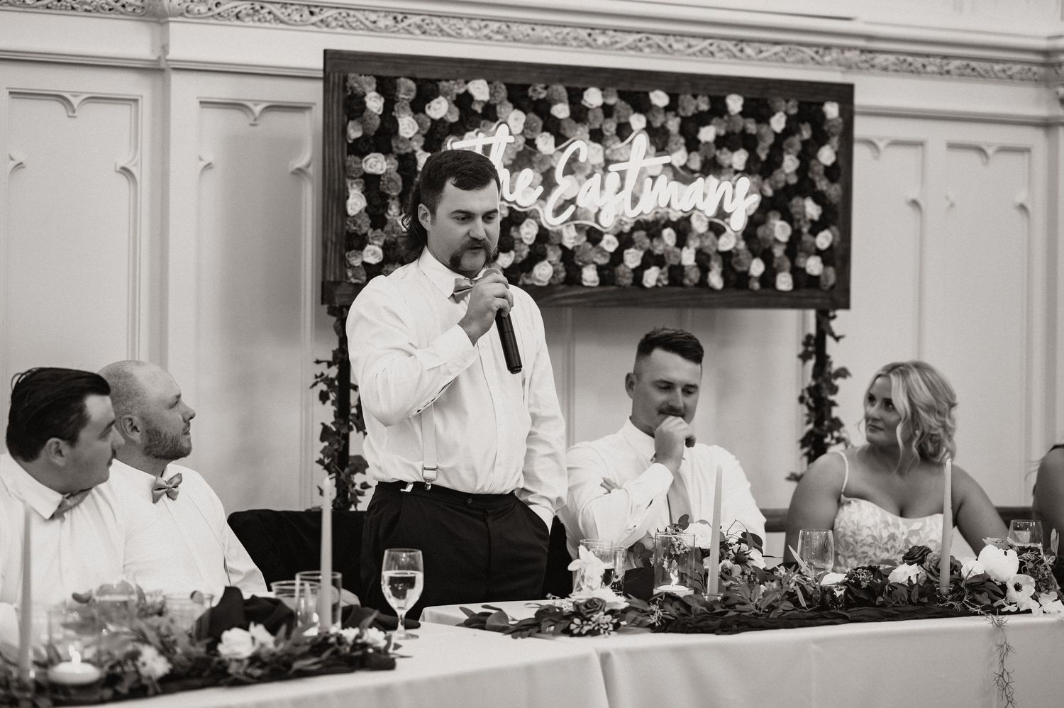 Black and white capture of wedding toasts at the head table during reception.