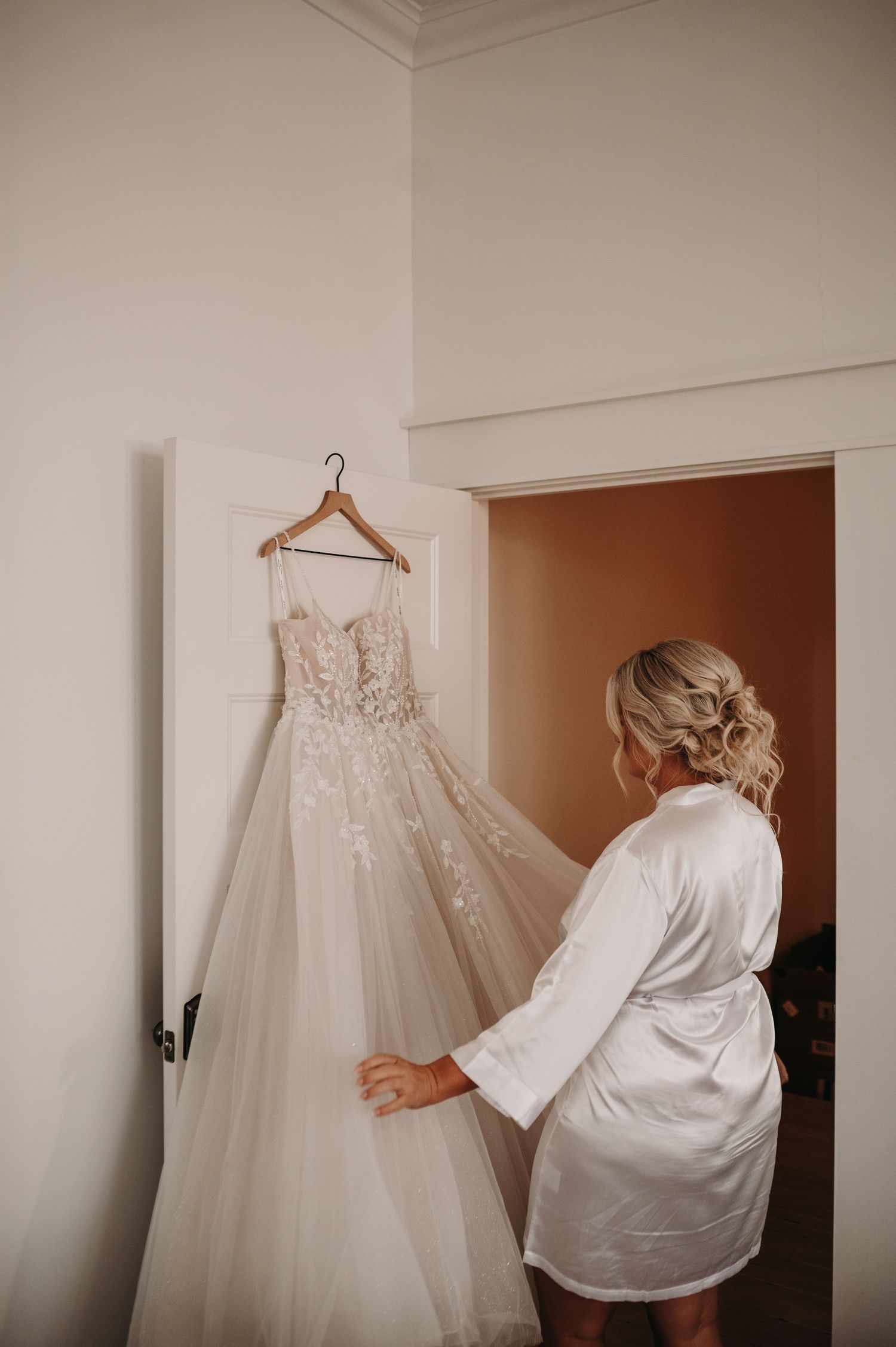 Beautiful white lace wedding dress hanging while being admired in preparation room.