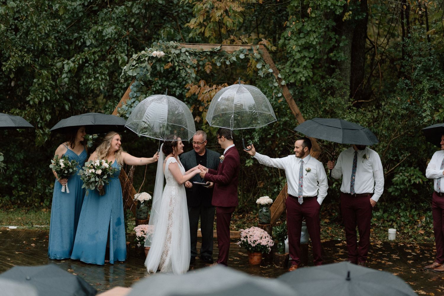 Wedding party with umbrellas gathered in a lush garden setting.