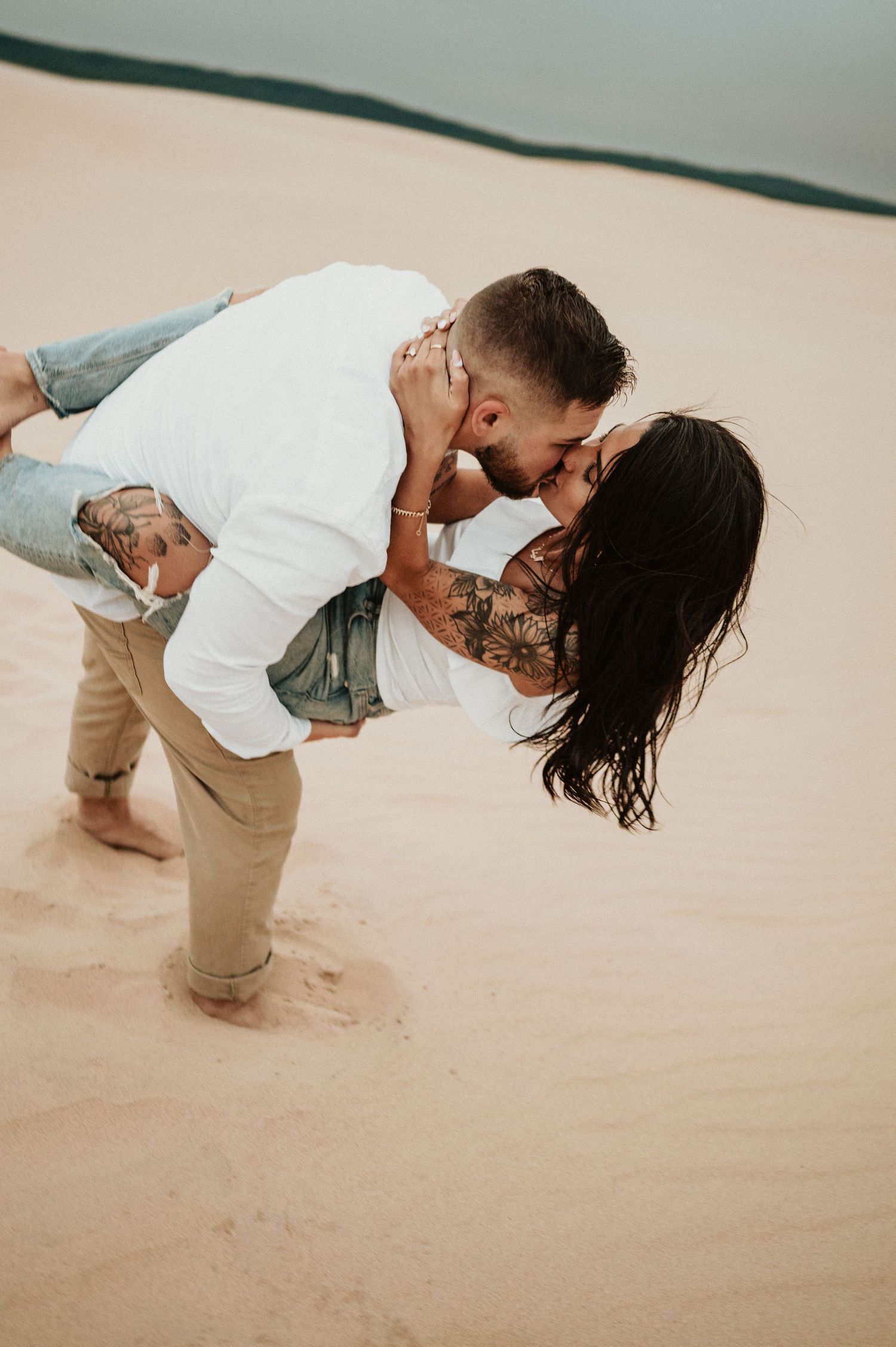 An intimate moment captured between a couple on sandy dunes during sunset.
