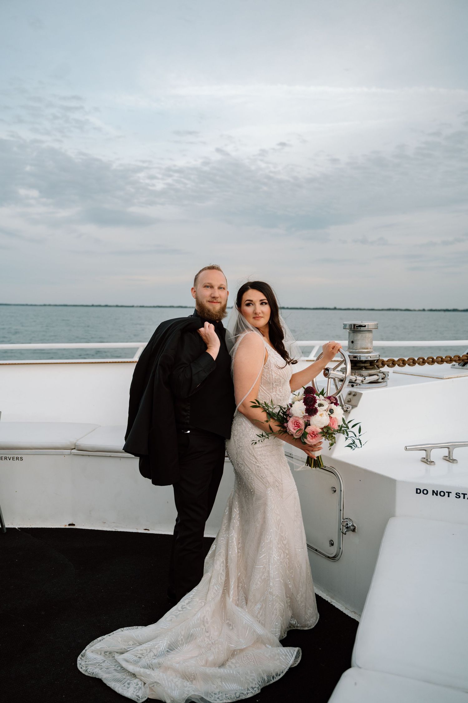 Wedding couple shares intimate moments aboard white yacht deck under cloudy skies.