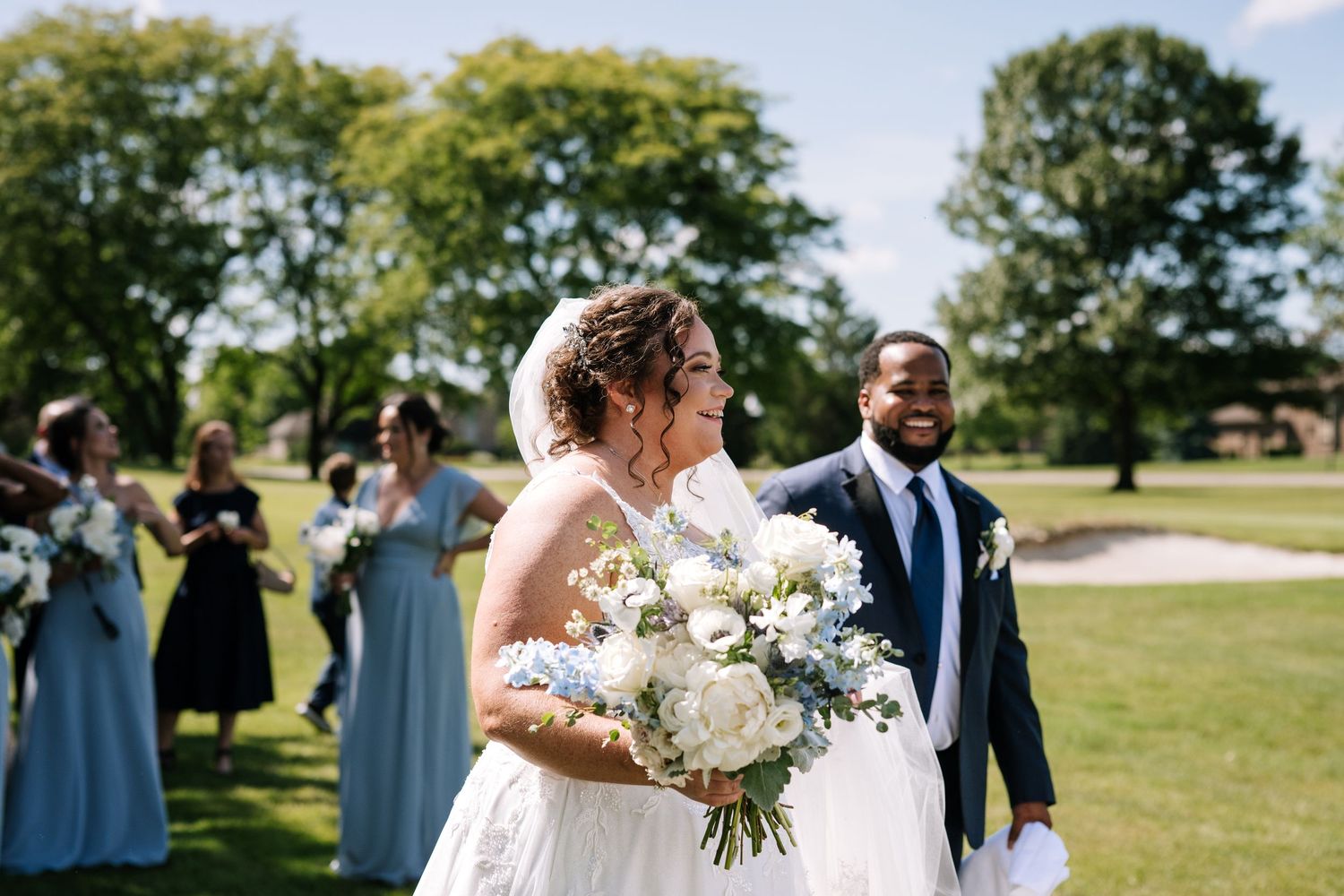 Outdoor wedding ceremony setup with white chairs and floral arrangements under blue sky.
