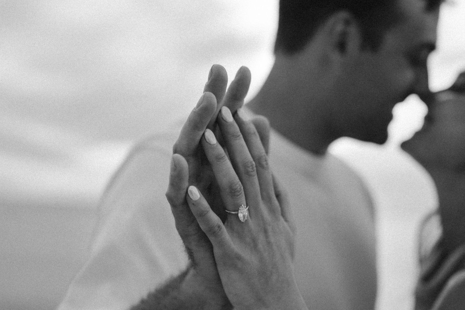 Black and white photo of couple holding hands showing engagement ring.