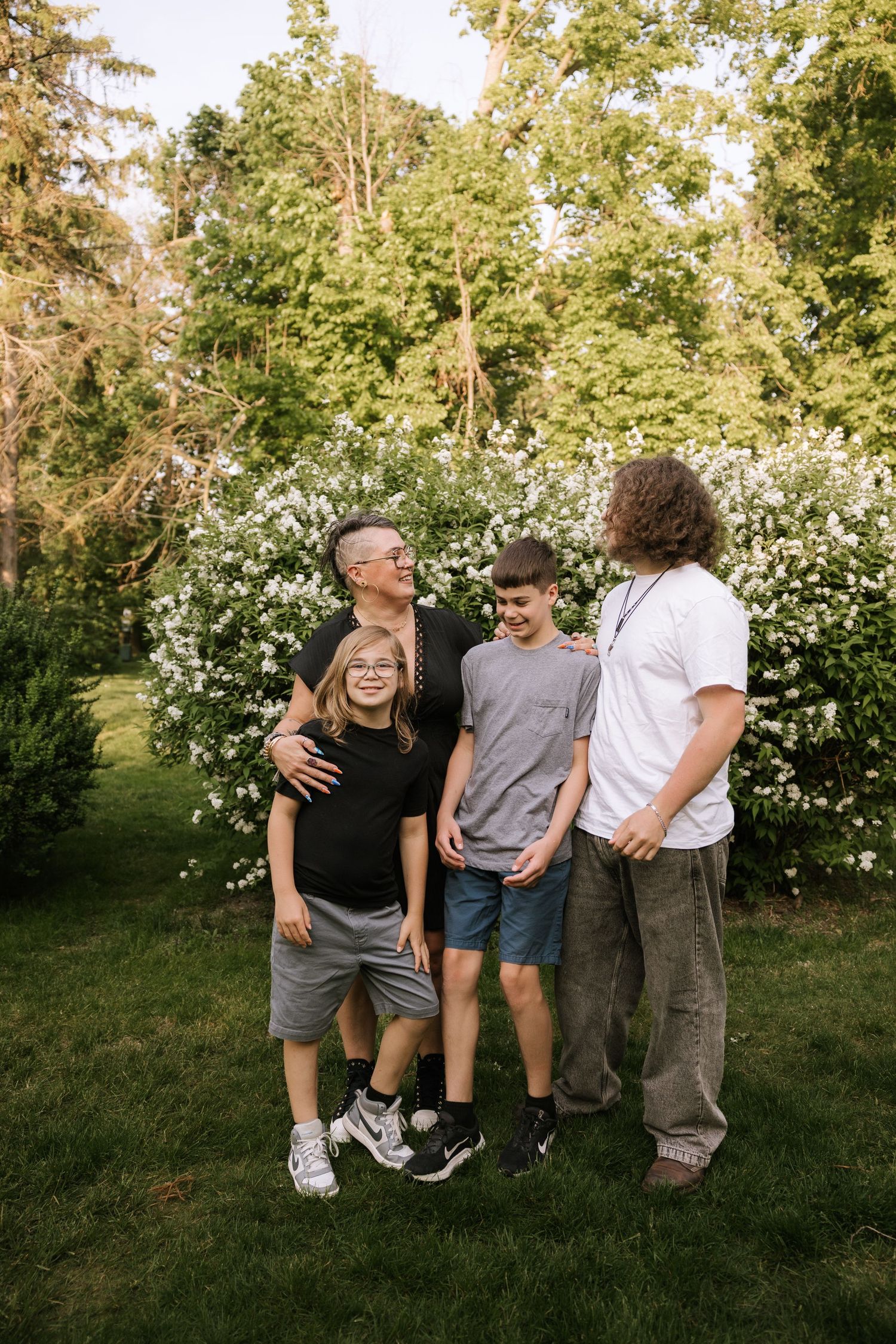 Father with three children laughing together in garden with white flowering bushes.