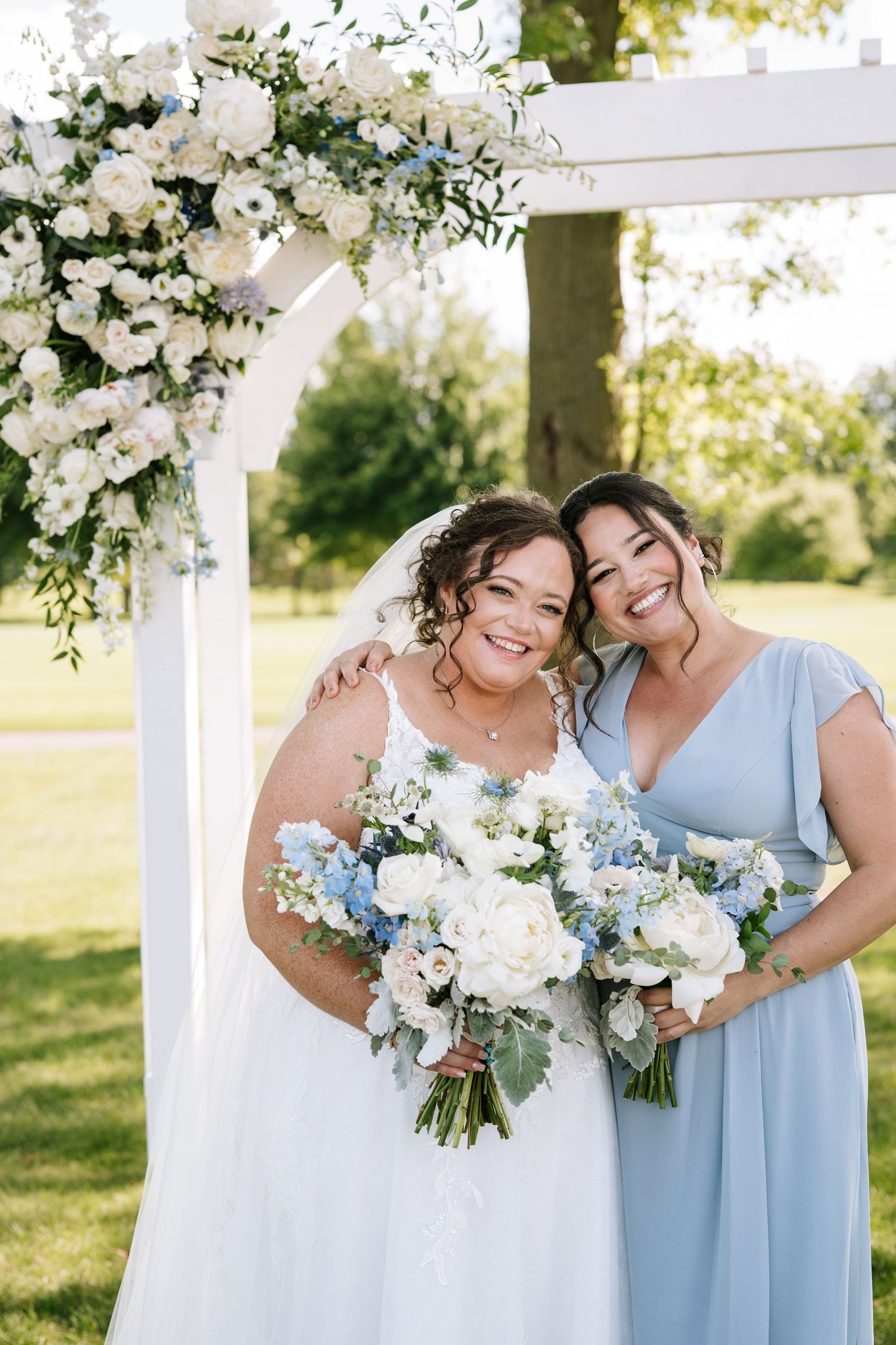 Beautiful floral arch with white and blue flowers decorates an outdoor wedding setting.