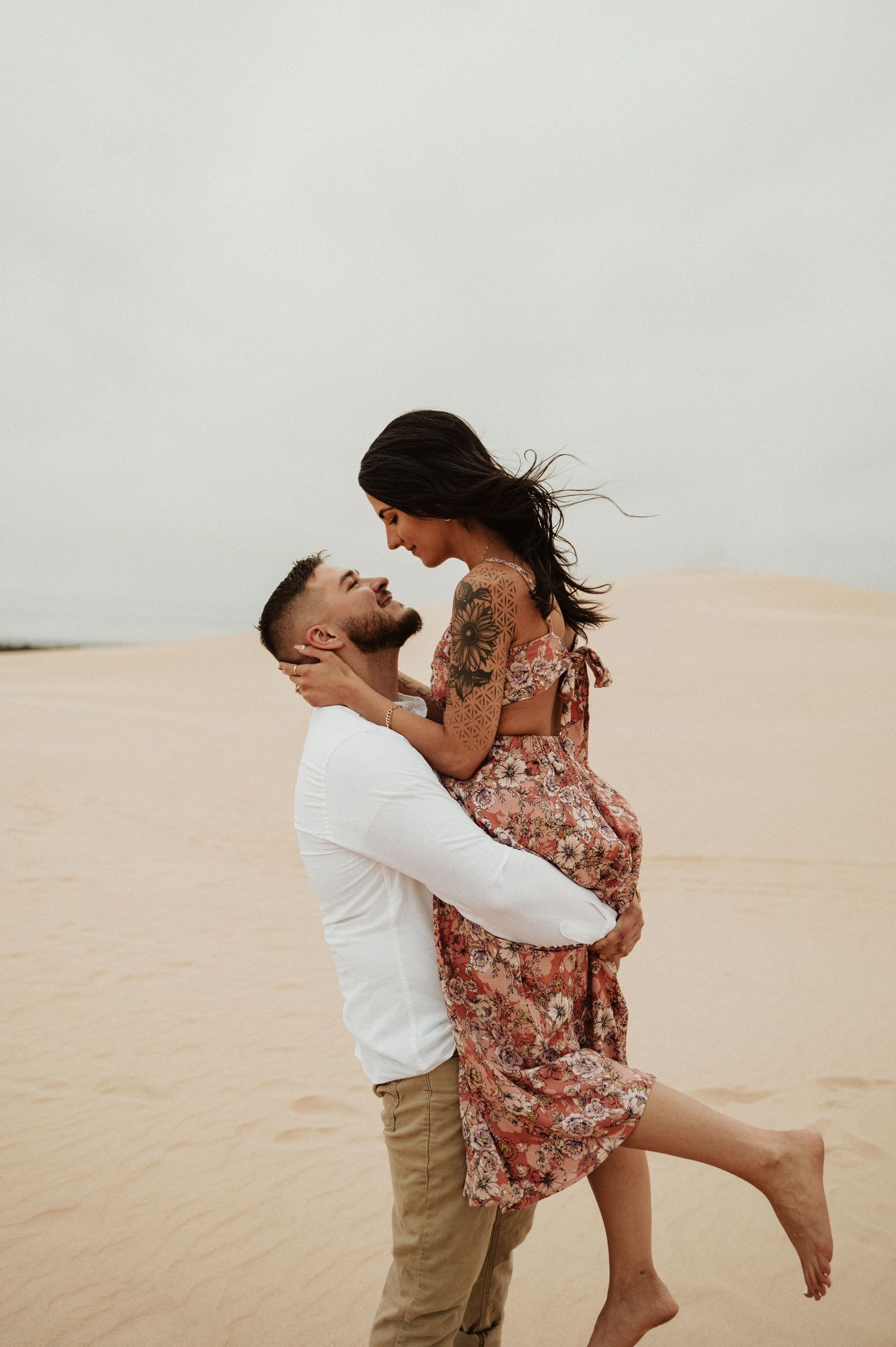 A romantic lift pose captured on sand dunes during an engagement session.