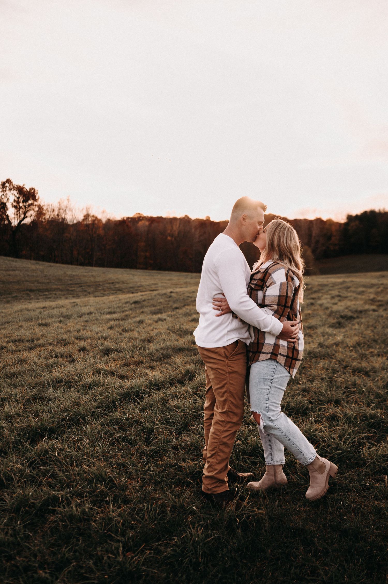 Romantic embrace in golden hour light on grassy hillside.