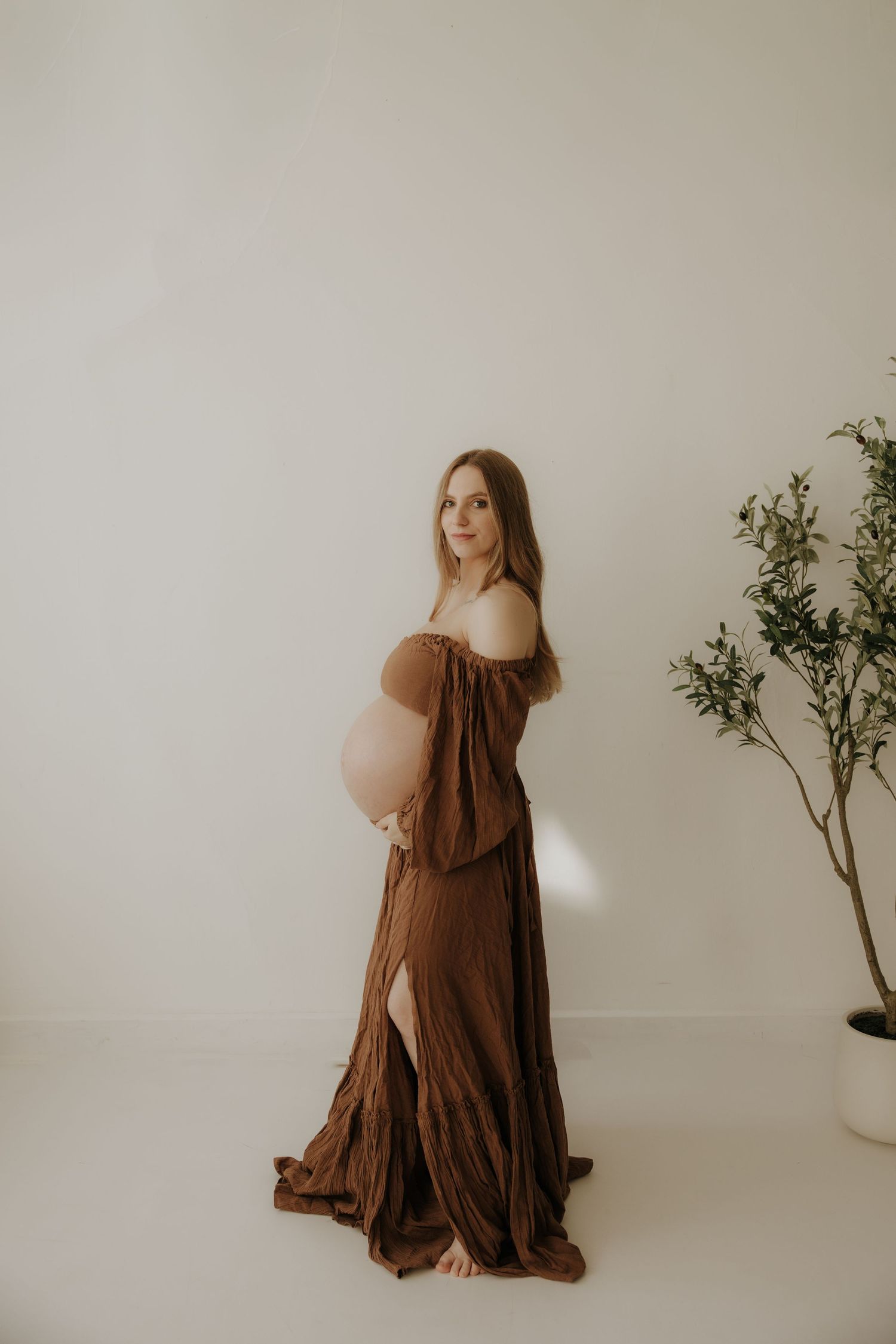 Maternity session featuring flowing brown dress against minimalist setting with greenery.