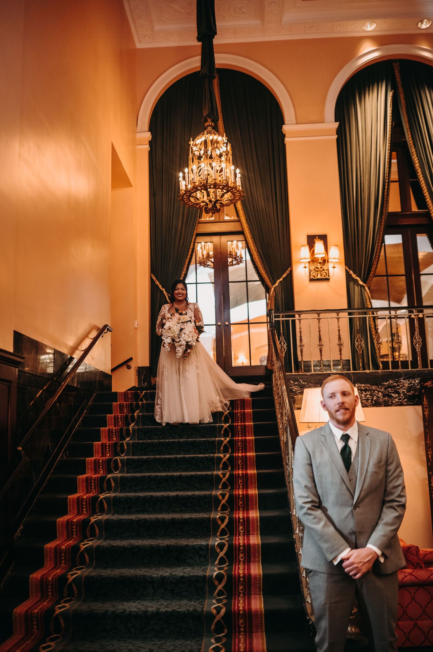 A grand staircase with red carpet and crystal chandelier in an elegant venue during a wedding.