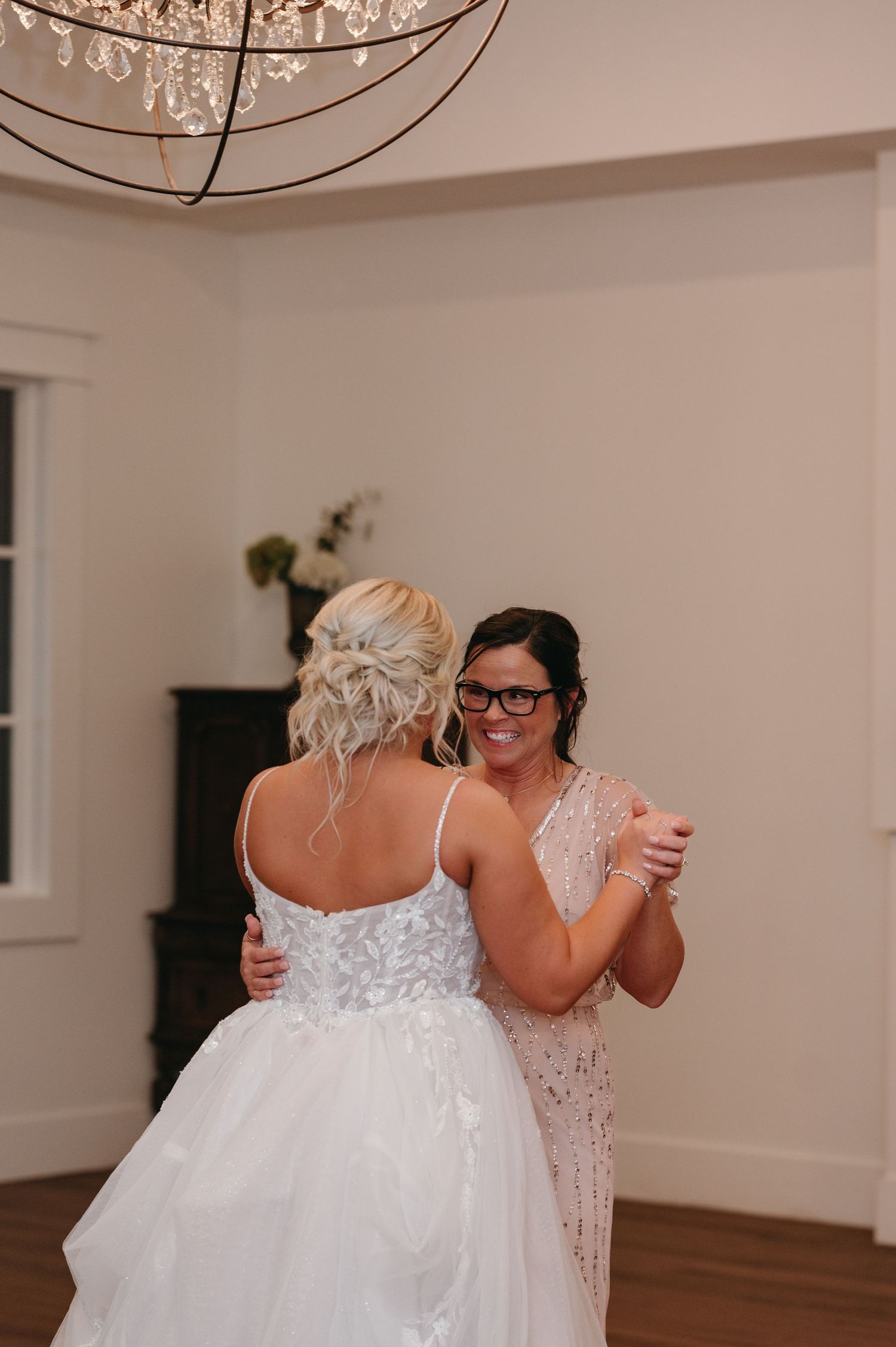 Emotional dance moment under crystal chandelier at wedding reception.