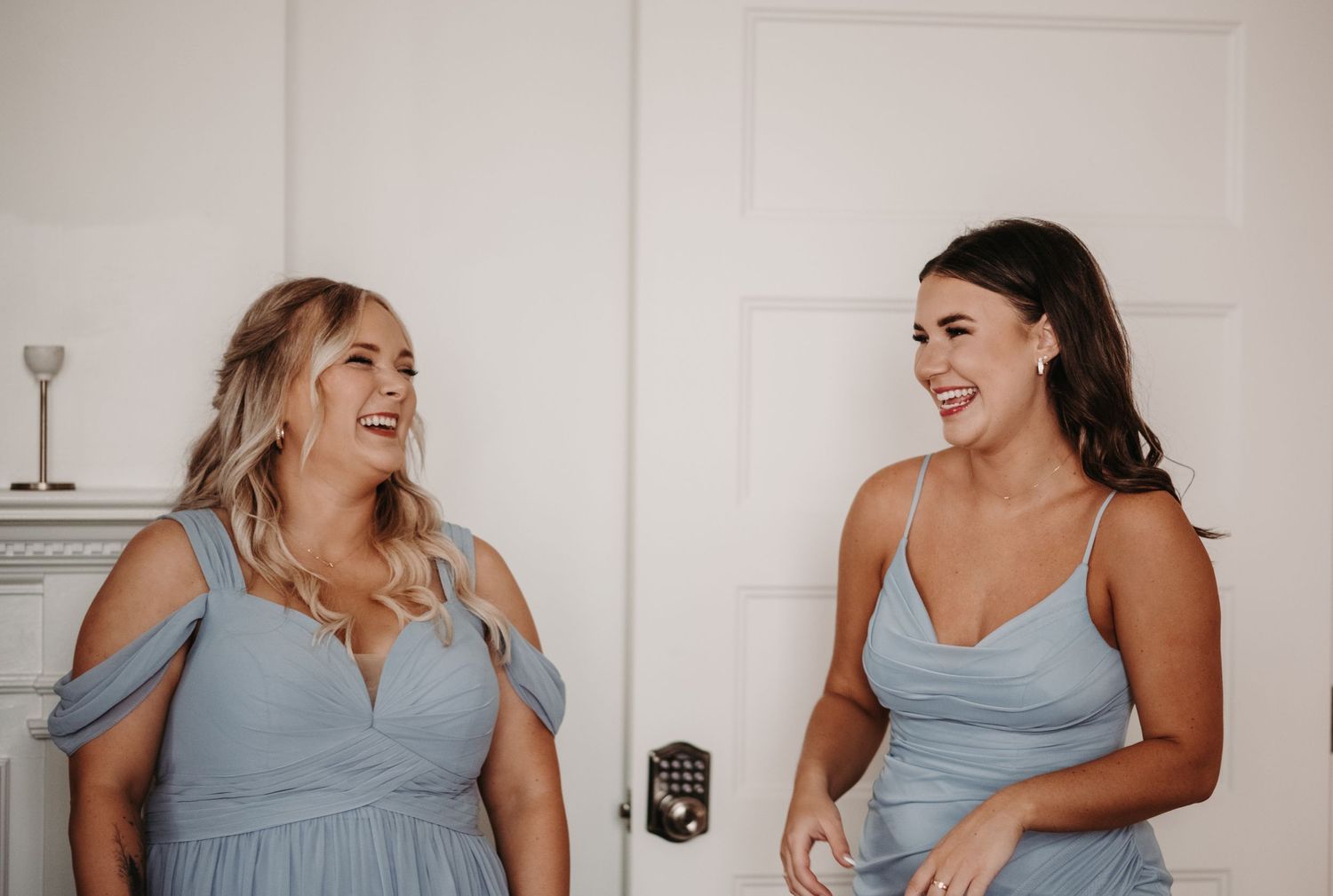 Two bridesmaids in light blue dresses share a candid laughing moment together.