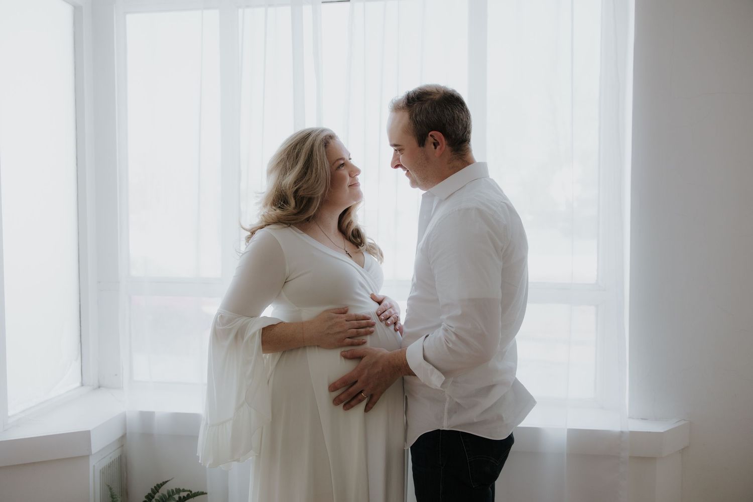 Intimate couple's photoshoot by large windows with bright natural light streaming in.