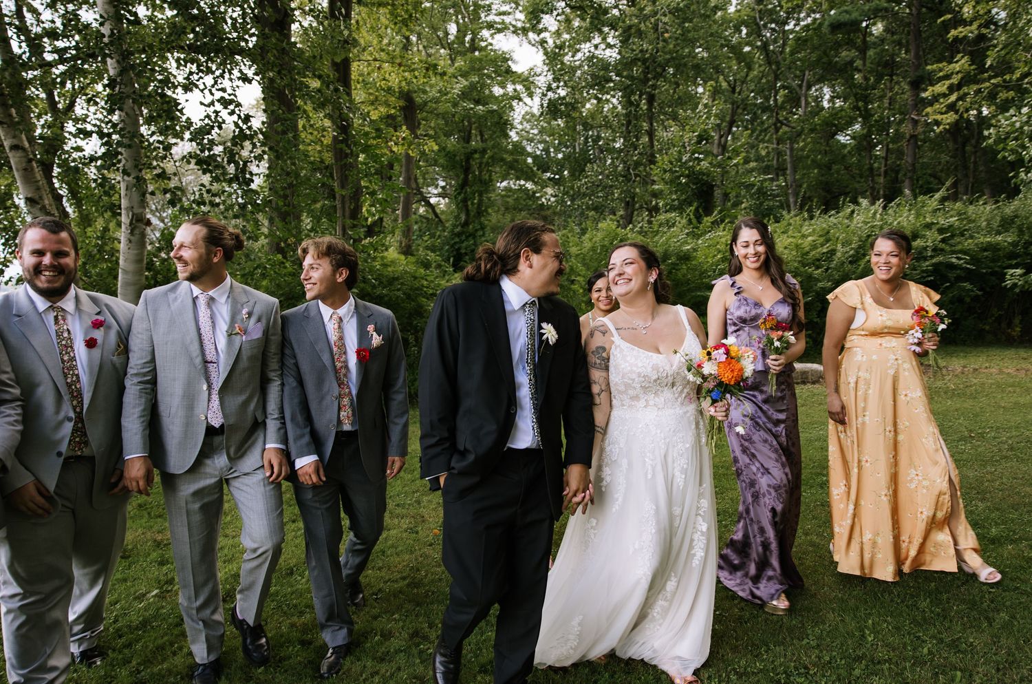Wedding party posing outdoors in formal attire with yellow bridesmaid dresses and grey suits.