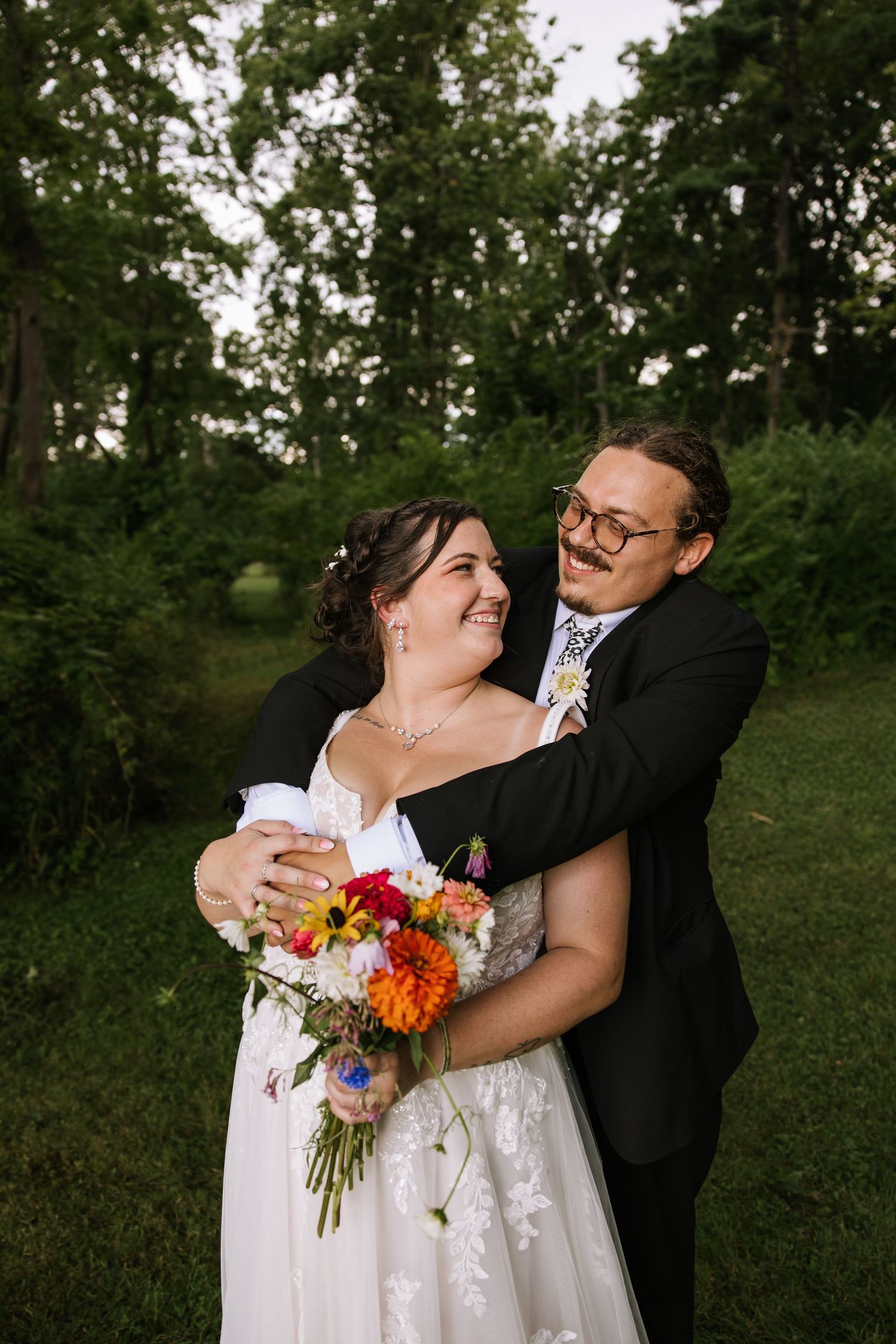 A couple shares joyful moments in an outdoor garden setting with colorful wedding bouquet and formal attire.