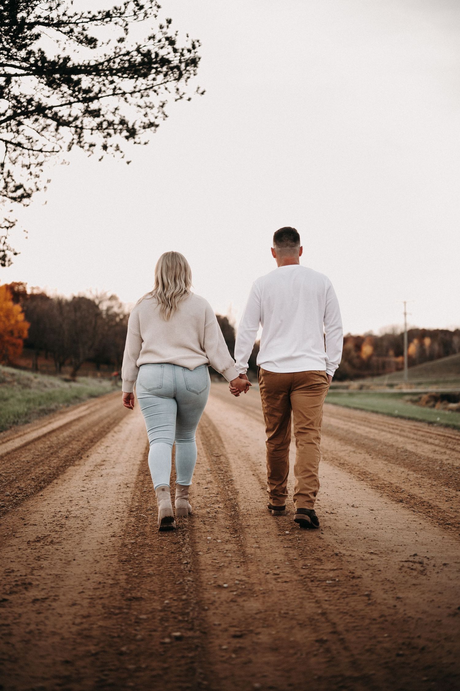 Couple walking hand in hand down a rustic dirt road during autumn.