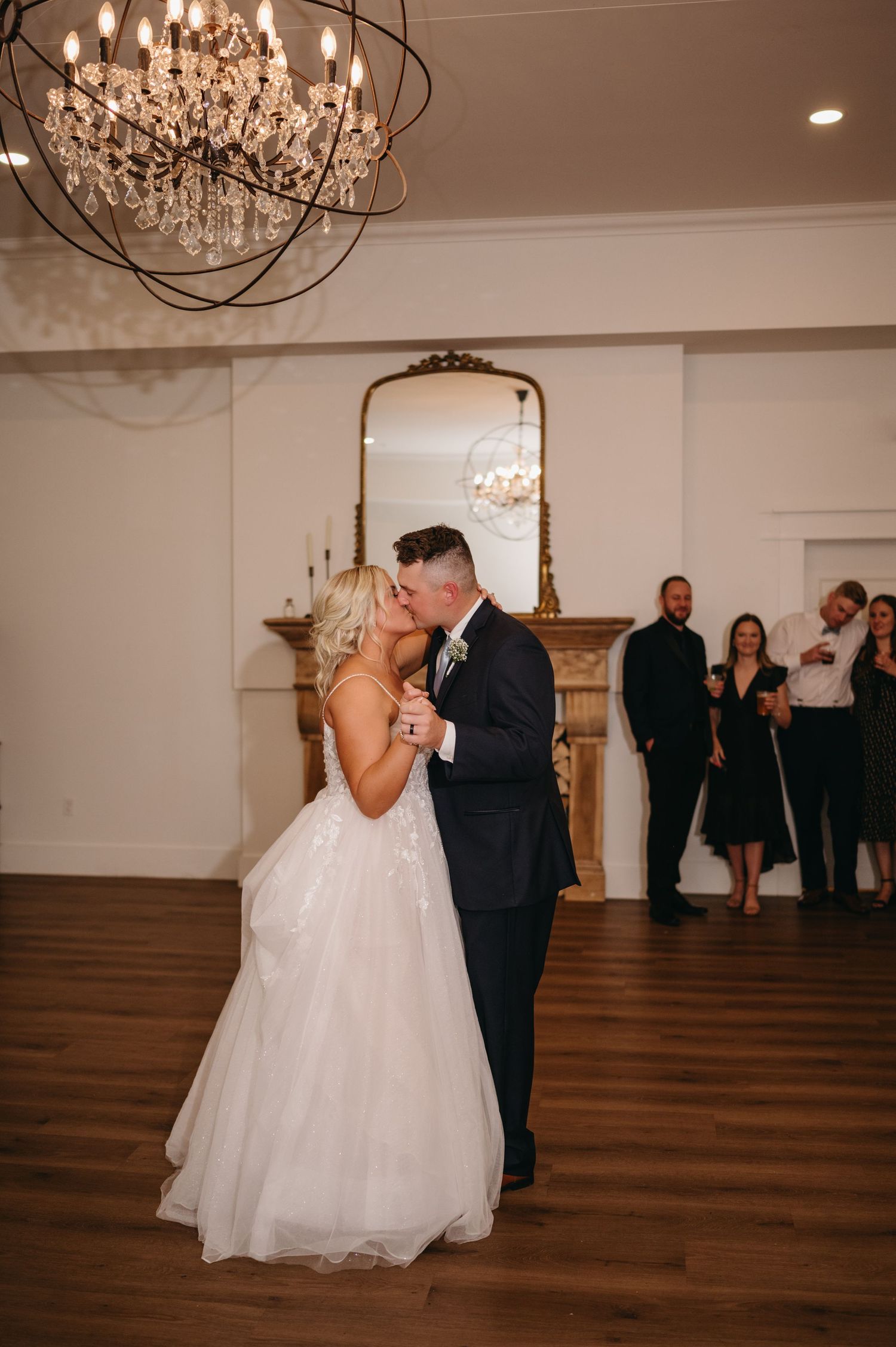 A romantic first dance moment under an ornate crystal chandelier at a wedding reception.