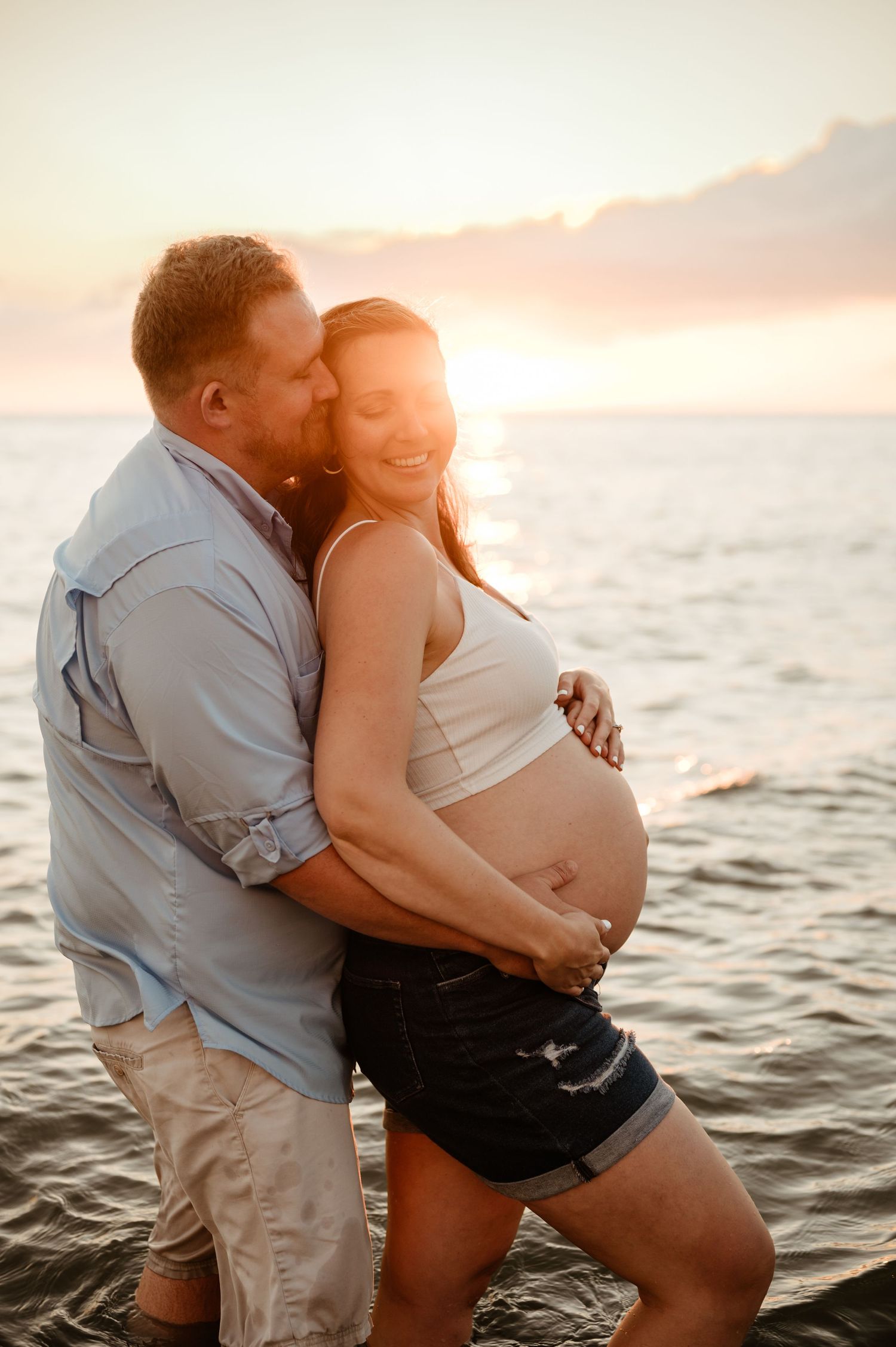 A couple shares an intimate moment on the beach at sunset as they celebrate an upcoming arrival.