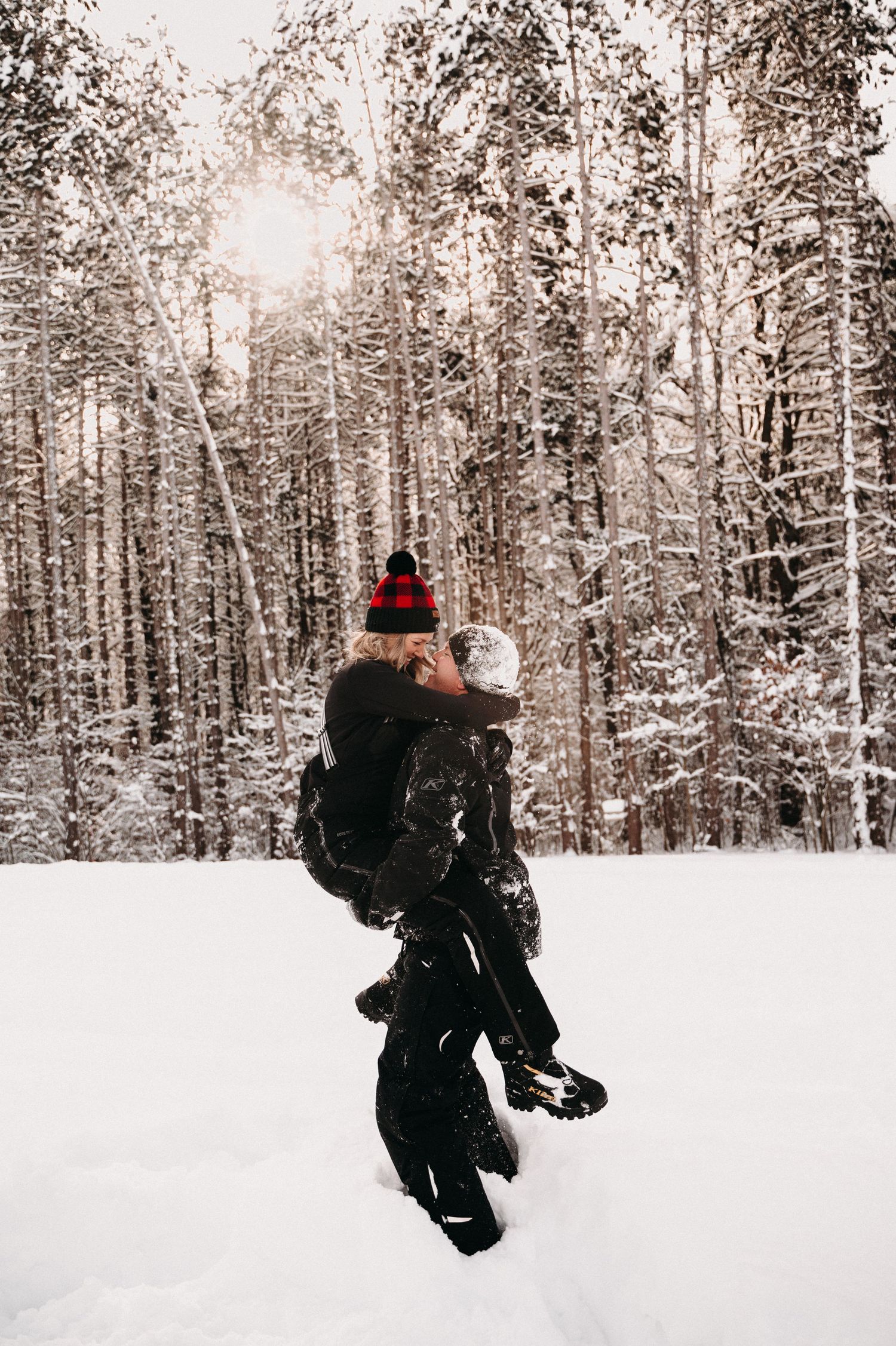 Person in black winter gear carrying someone through snowy forest.