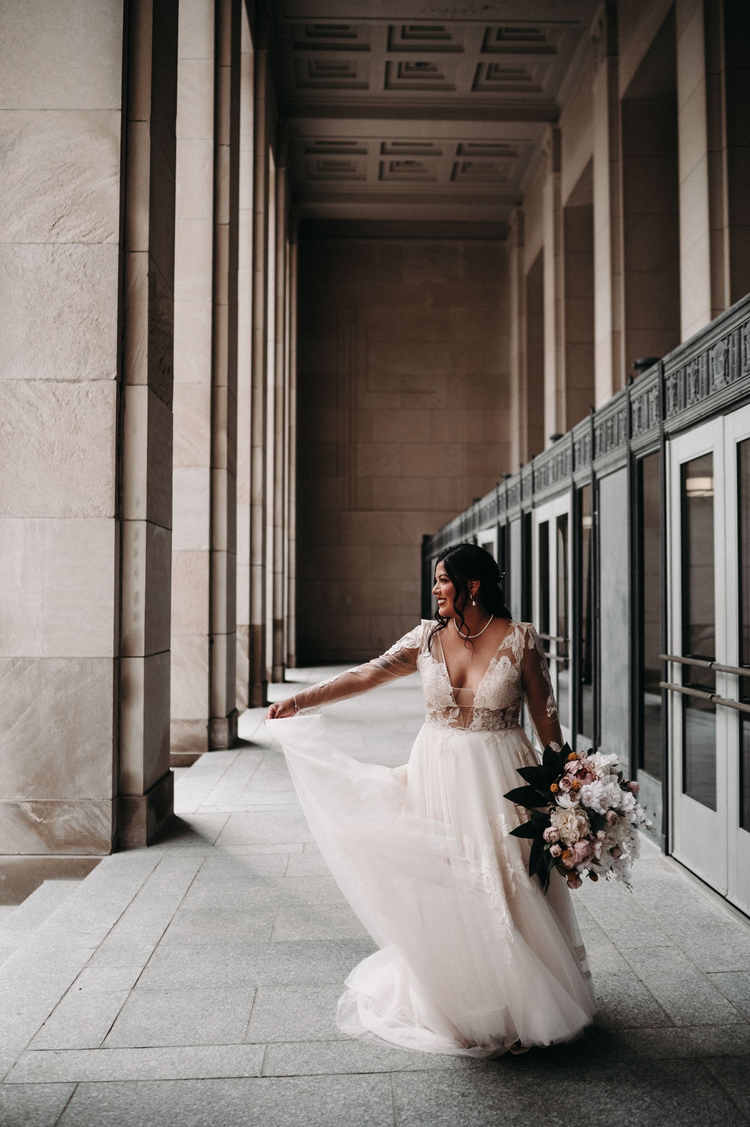Bride twirls her flowing white dress in an elegant stone hallway with tall columns.