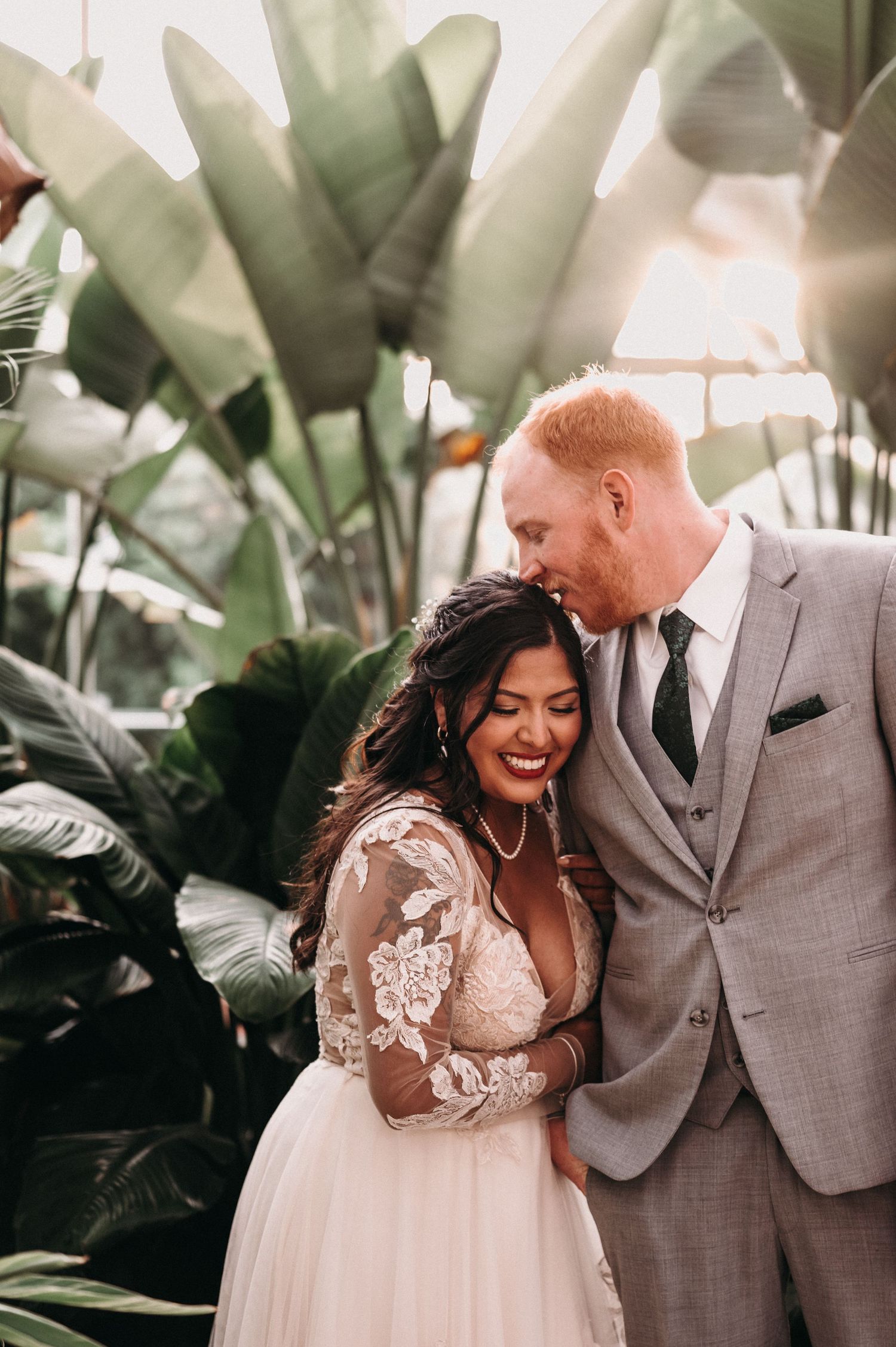 Joyful wedding couple shares an intimate moment among tropical greenhouse plants.