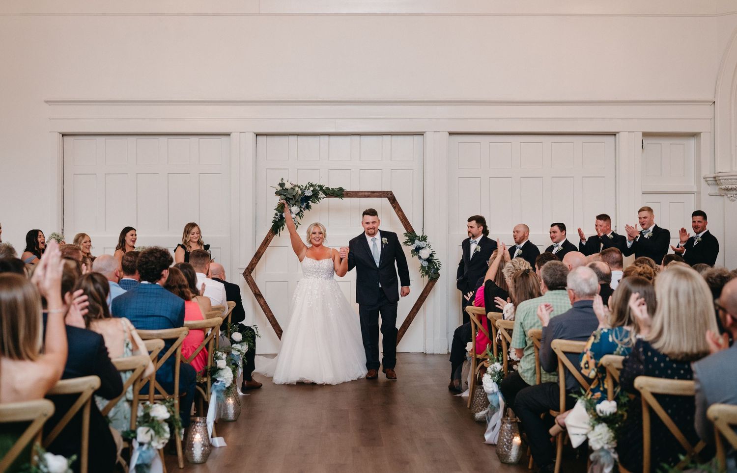 Wedding celebration in a modern venue with geometric arch and seated guests in casual attire.