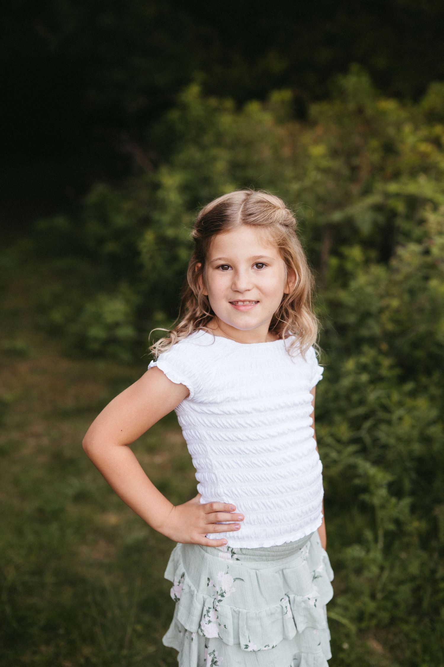 A confident pose in a white top and mint skirt against a natural backdrop.