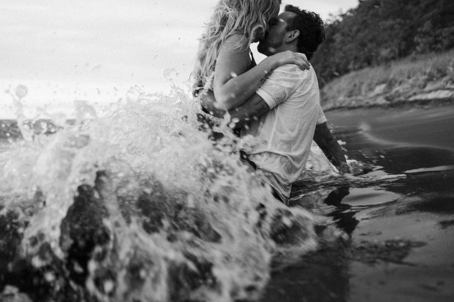 Ocean waves crash dramatically against rocky shoreline in black and white.