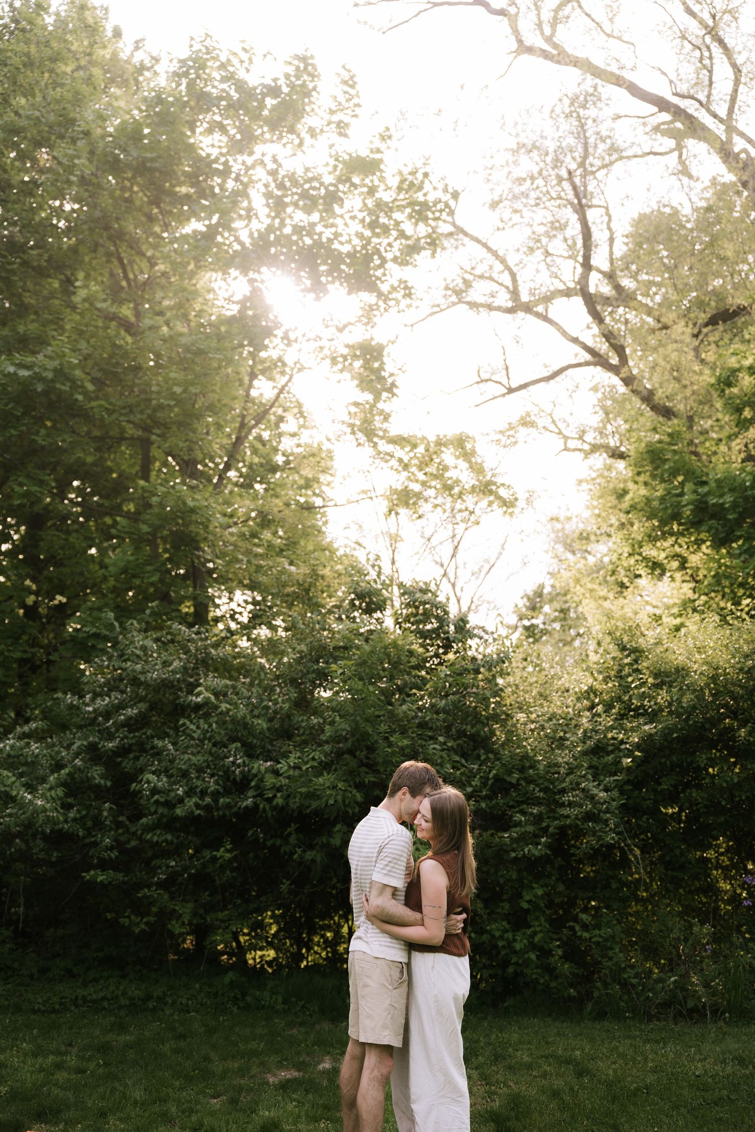 Romantic couple embracing in golden sunlit garden surrounded by green trees.