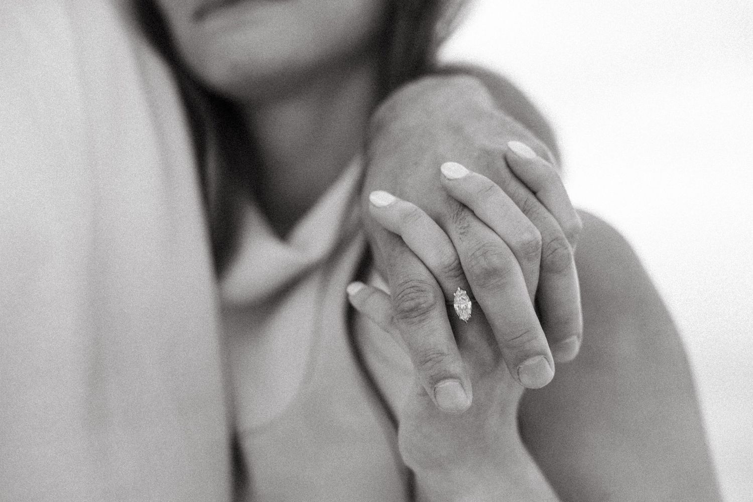 Close-up black and white photo of couple holding hands, showcasing a diamond engagement ring.