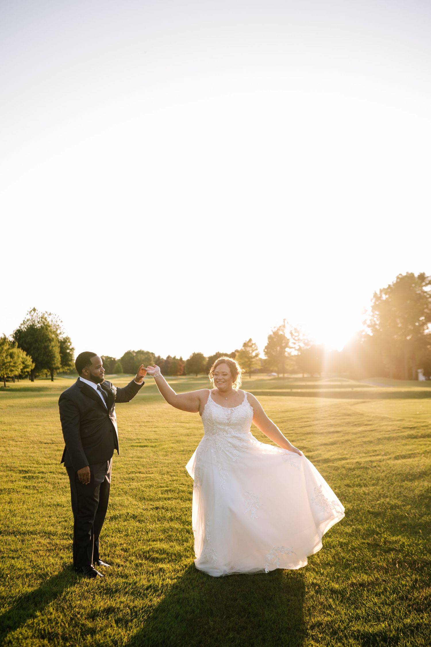 A wedding couple dances and twirls in a golden sunset field with flowing white dress.