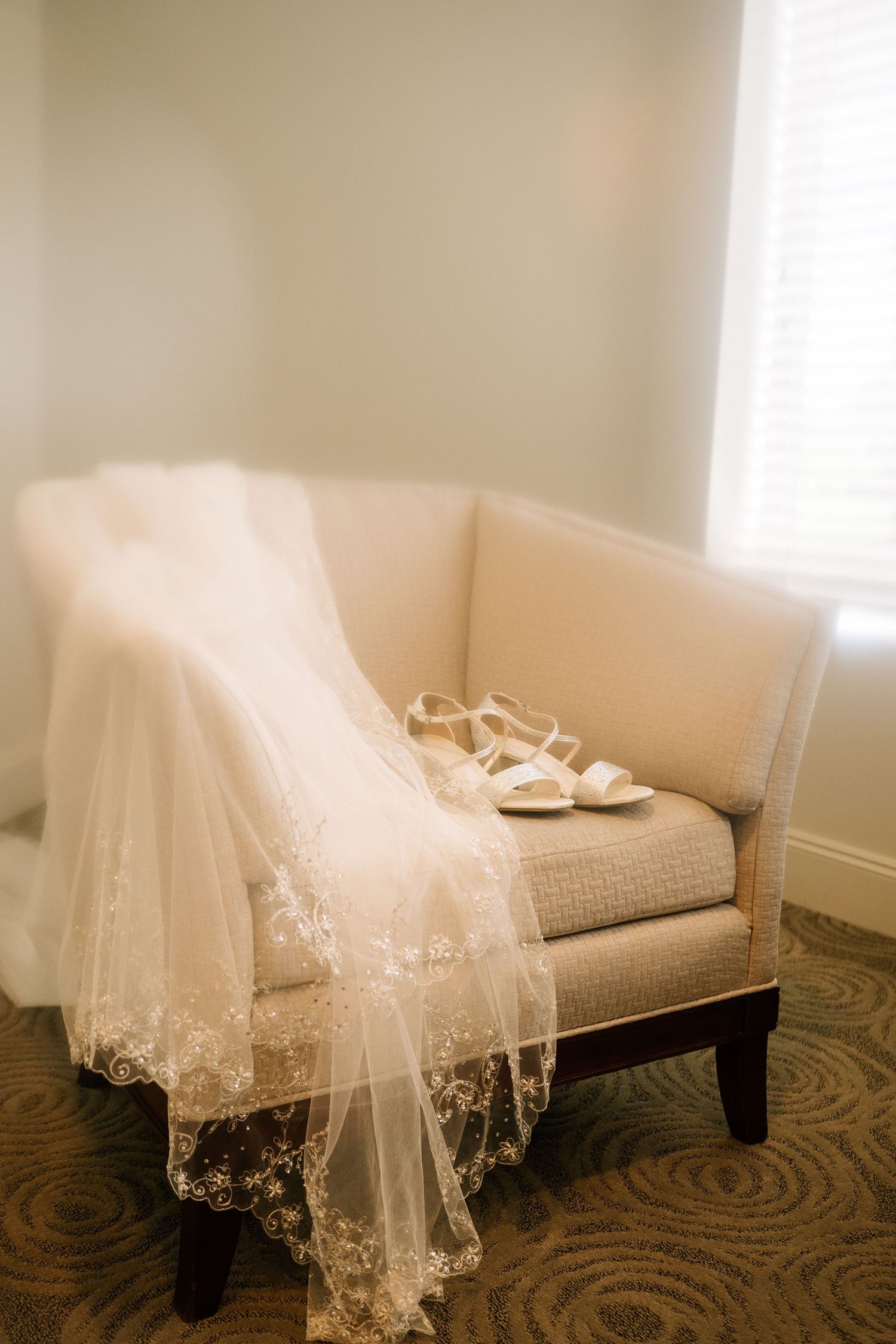 Delicate lace wedding veil with intricate embroidery detail draped over a beige couch in natural light.
