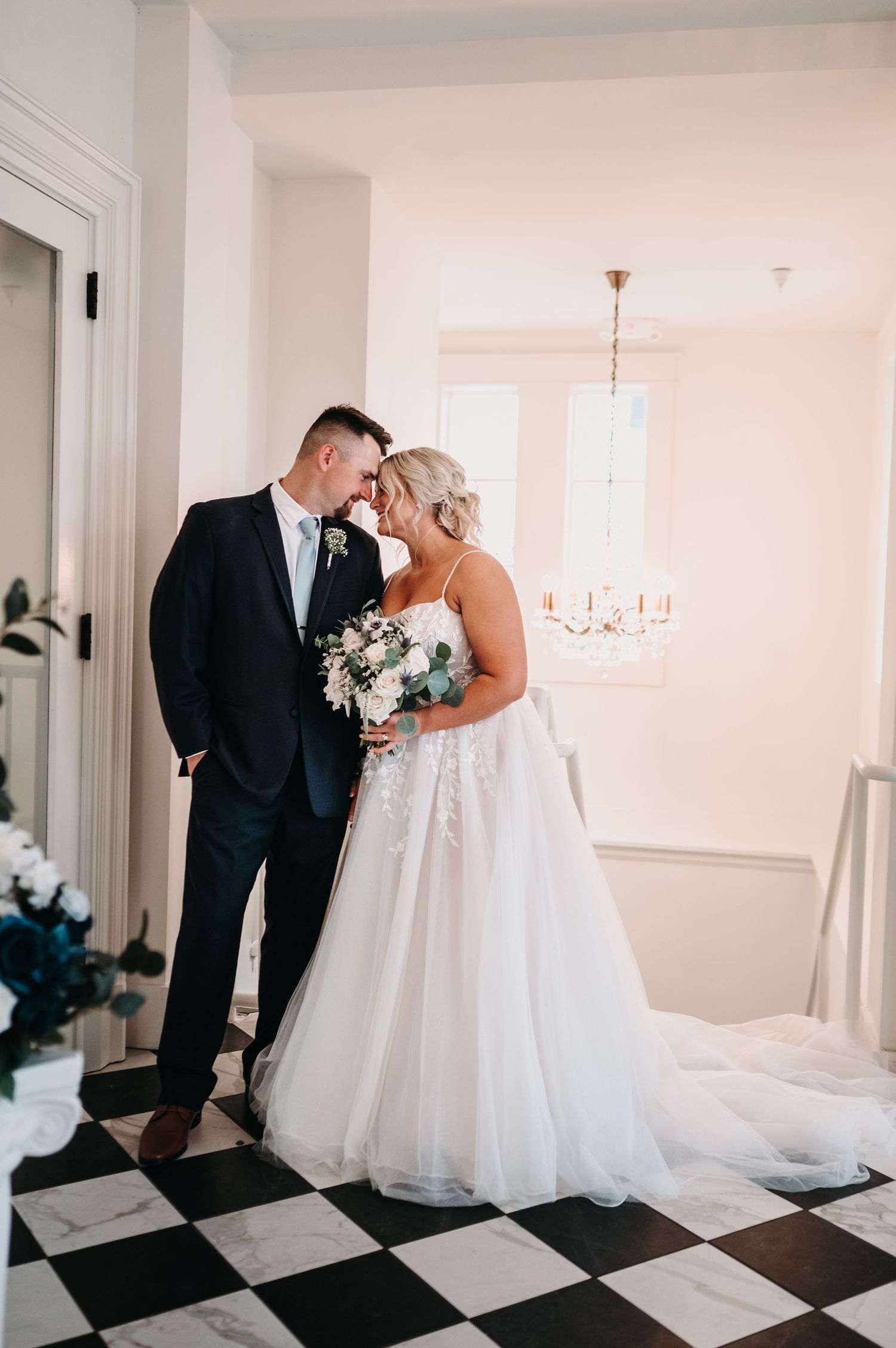 A tender moment captured between a couple on a checkered floor with elegant floral arrangements.