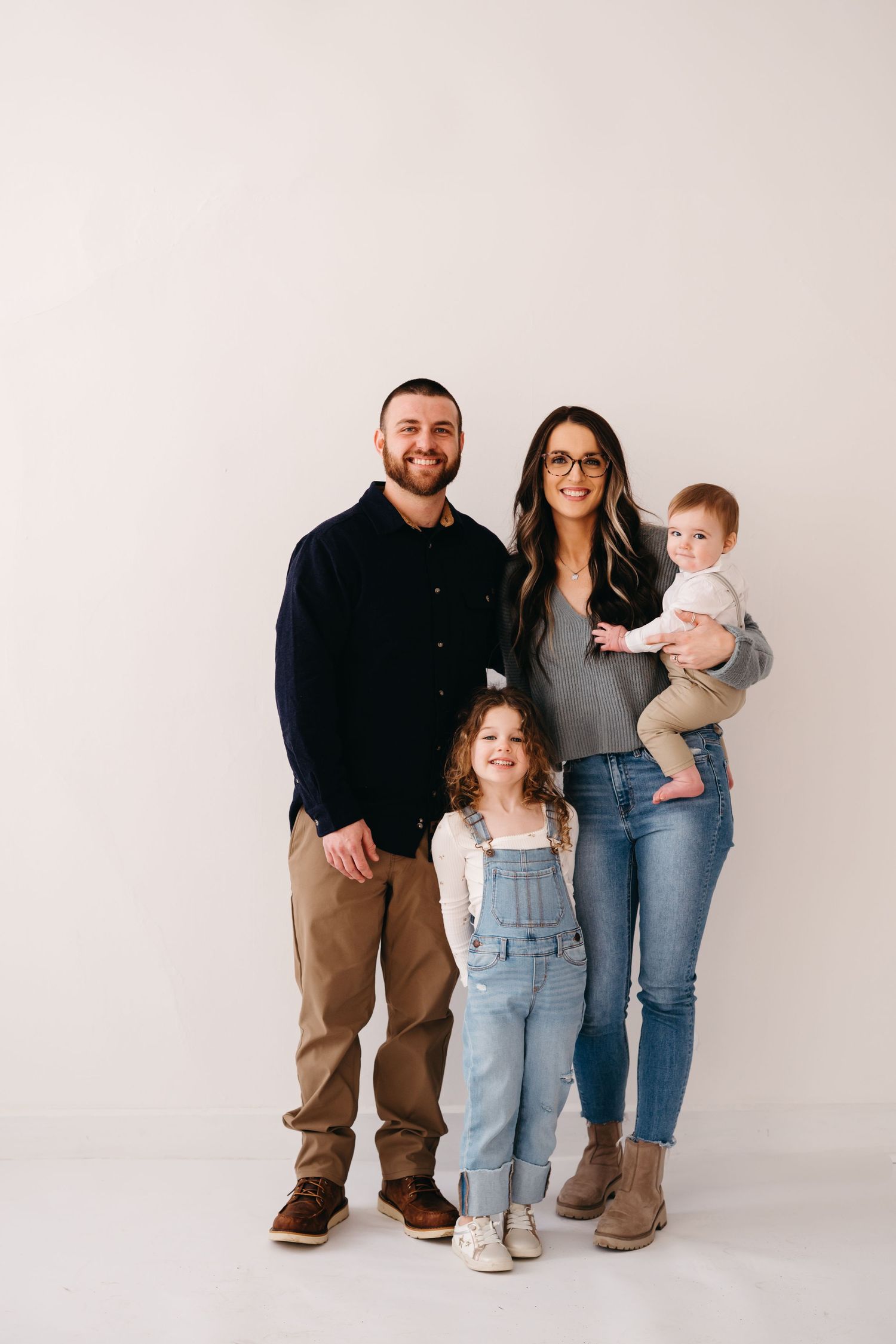 Modern family portrait against minimalist white backdrop in casual clothing.