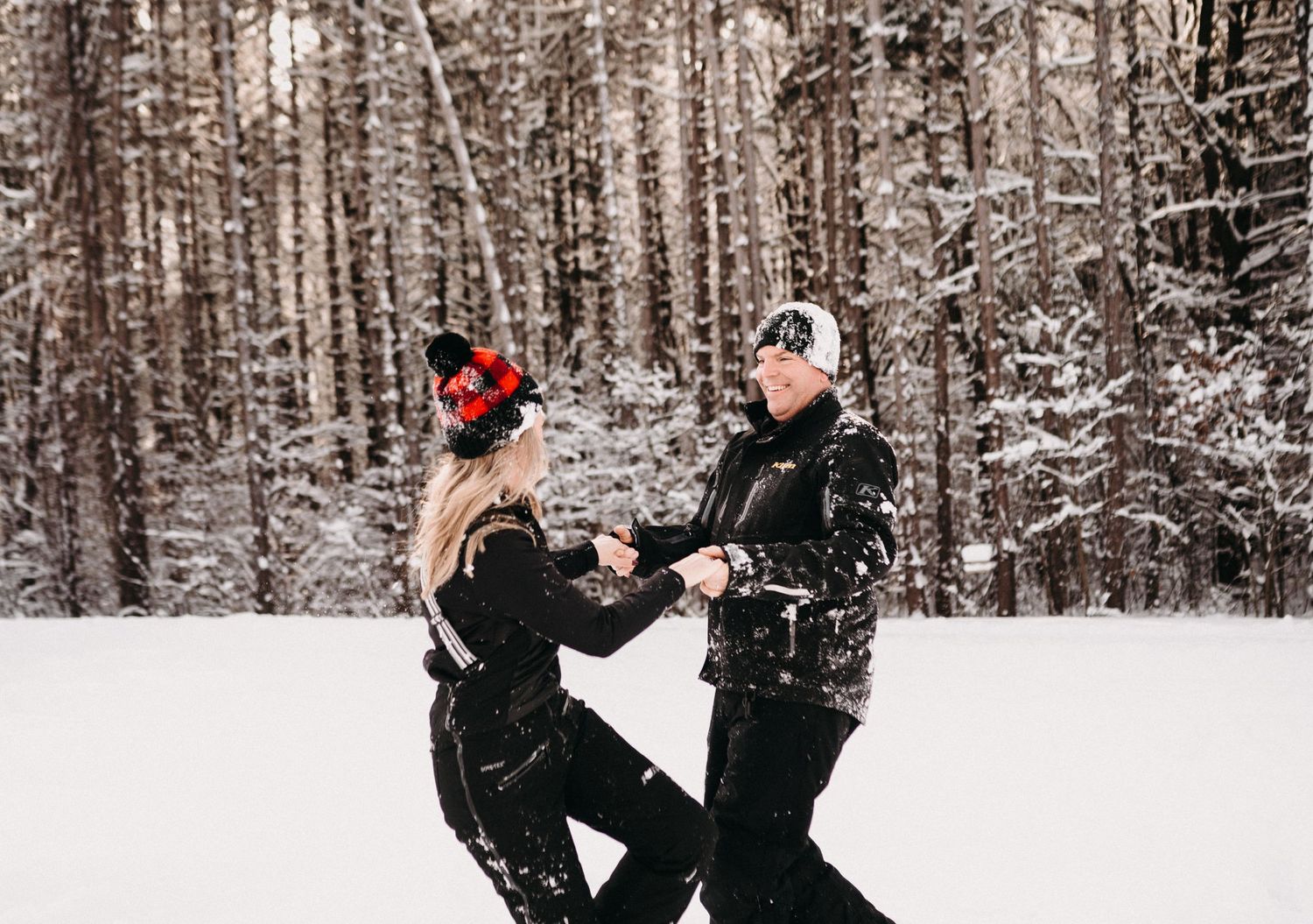 A winter proposal scene with two people in black winter gear surrounded by snowy trees.