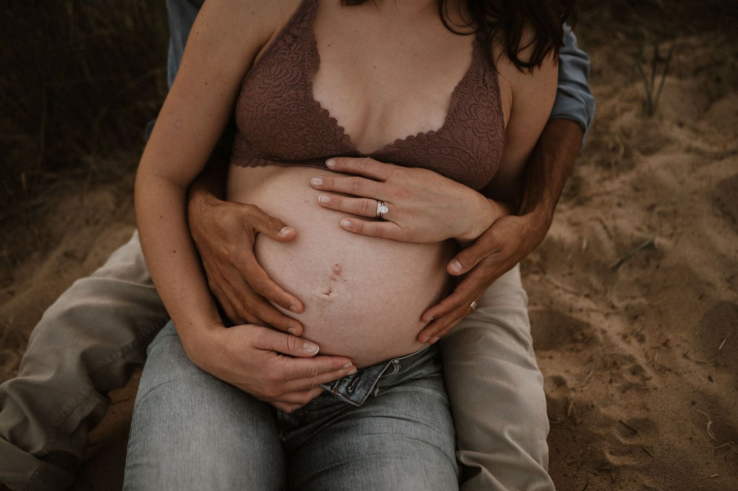 Close-up shot of hands tenderly cradling pregnant belly against sandy background.