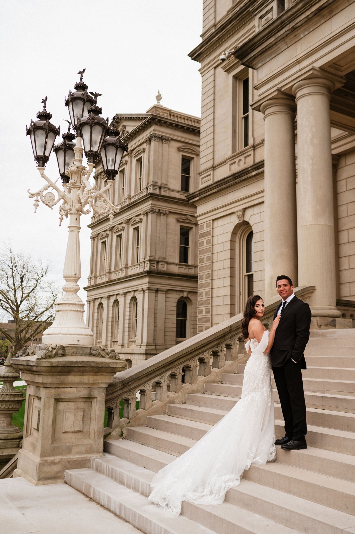 Wedding couple poses on ornate stone steps with decorative lamp posts.