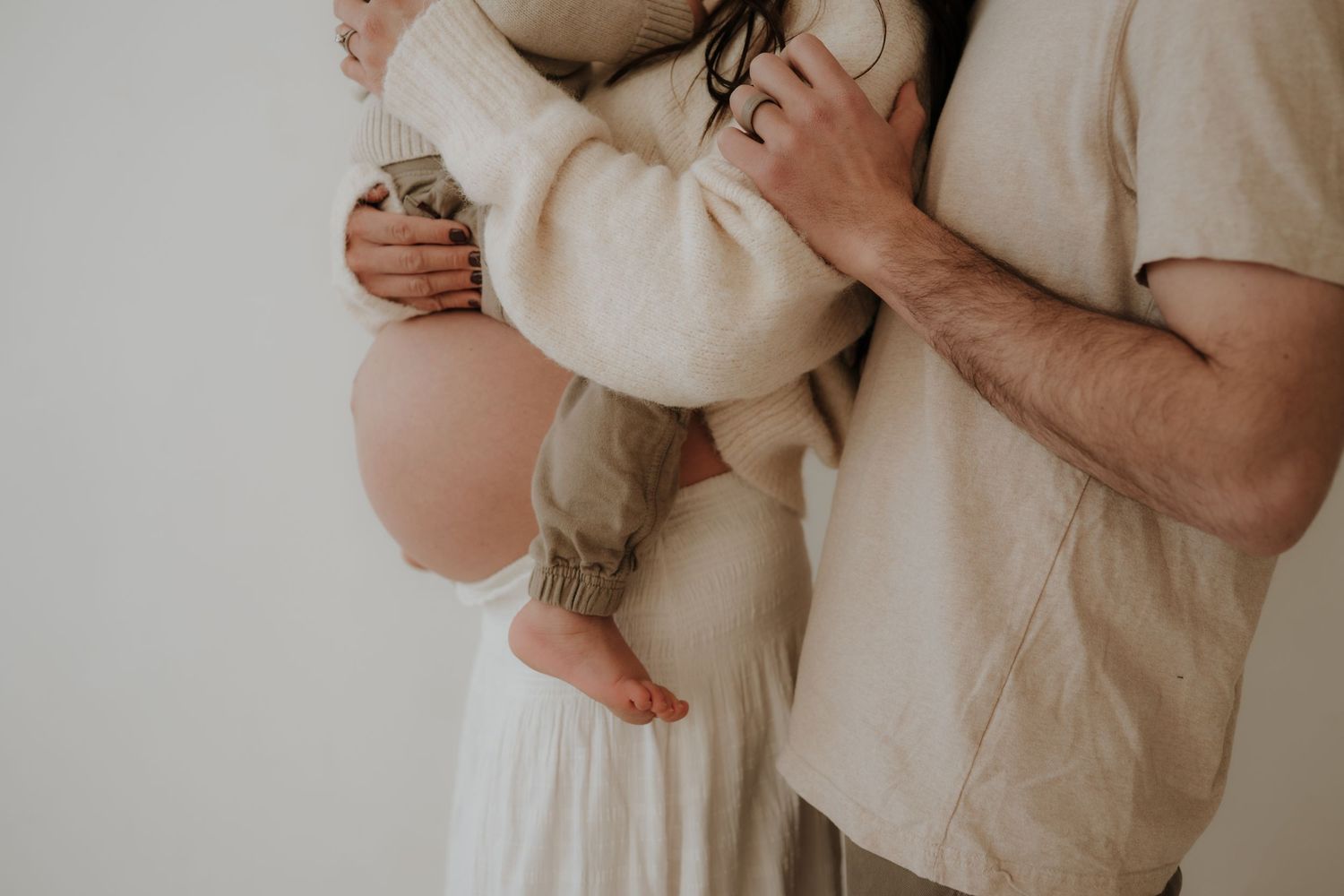 A tender family moment showing hands holding a baby in soft, neutral tones.