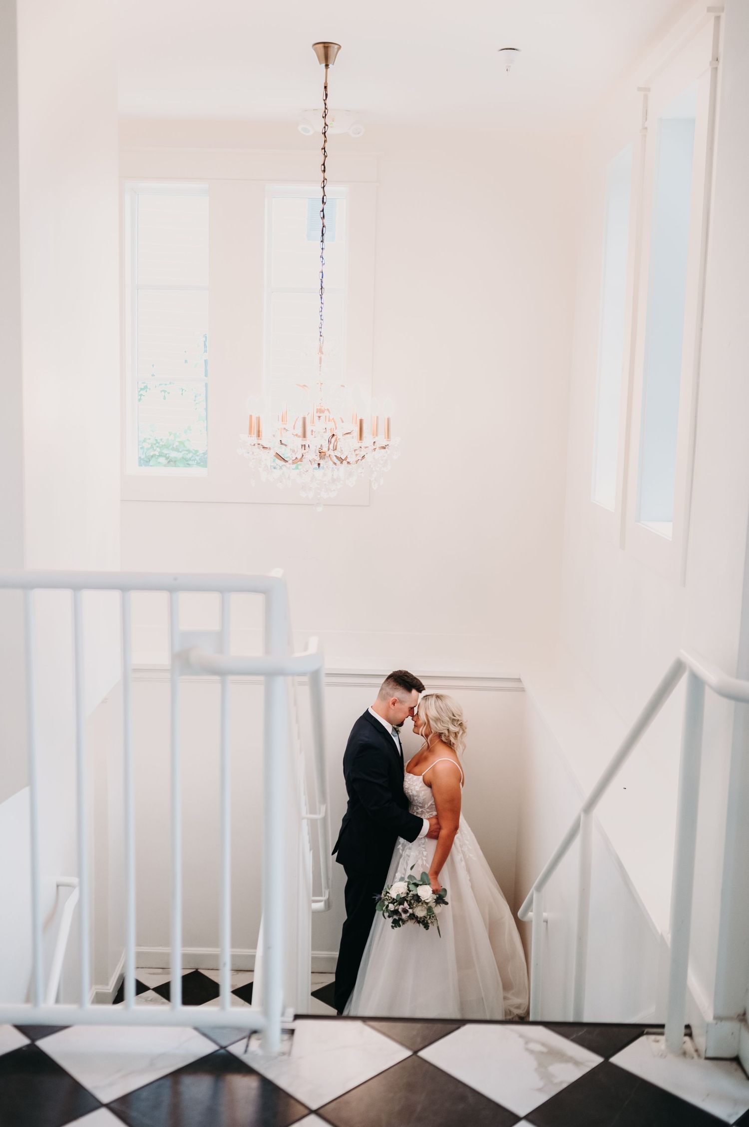 A romantic wedding moment captured on a black and white checkered floor beneath an elegant chandelier.