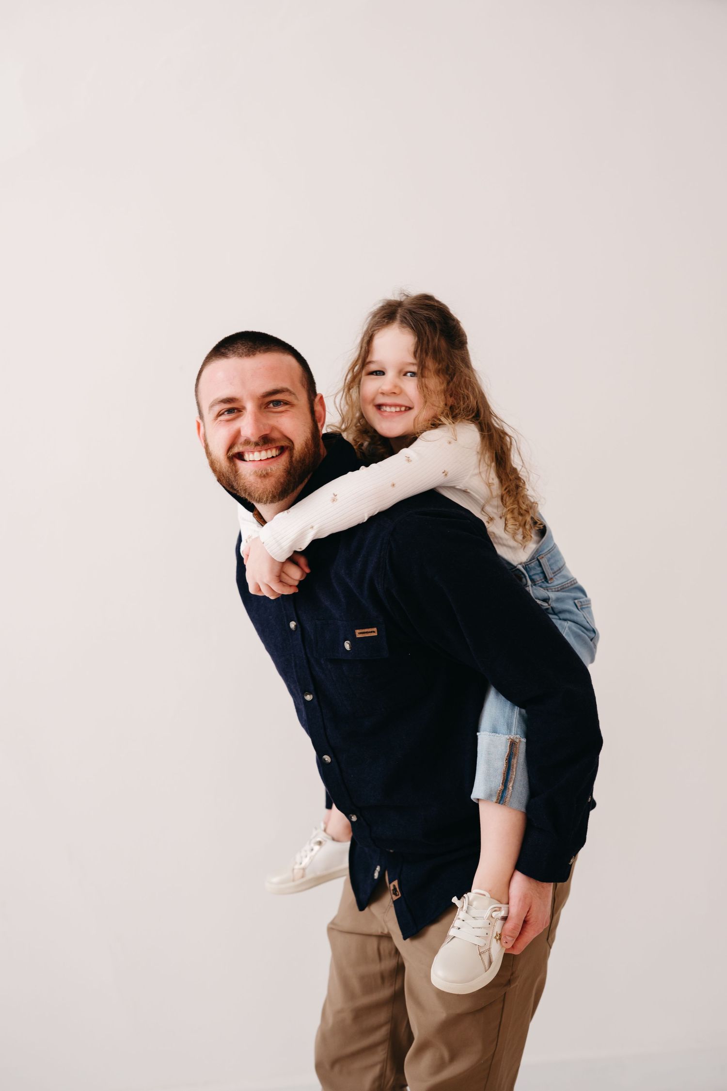 A heartwarming piggyback pose against a plain backdrop shows a playful parent-child moment.