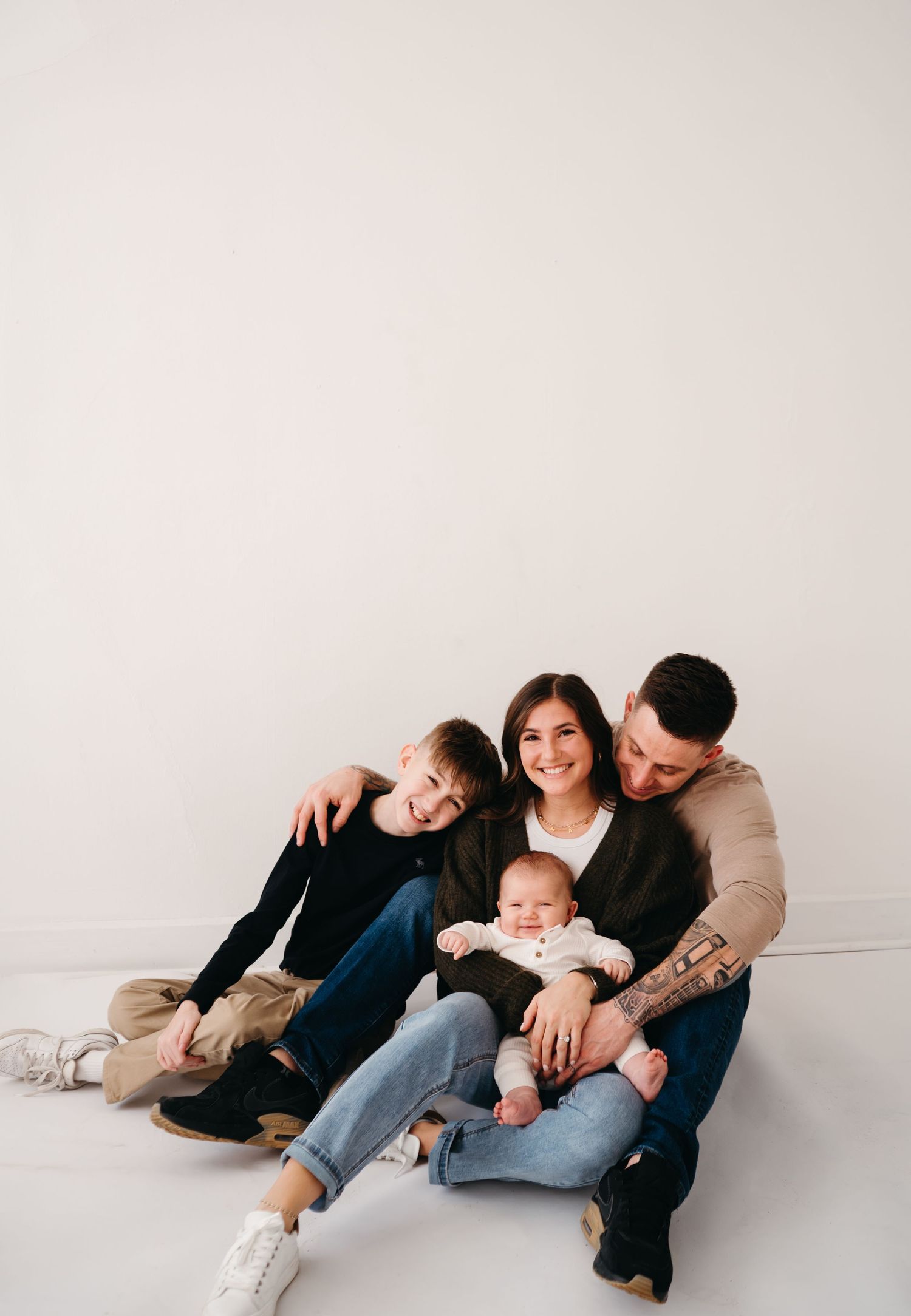 A happy family with a baby and child relaxes together on a white studio floor.