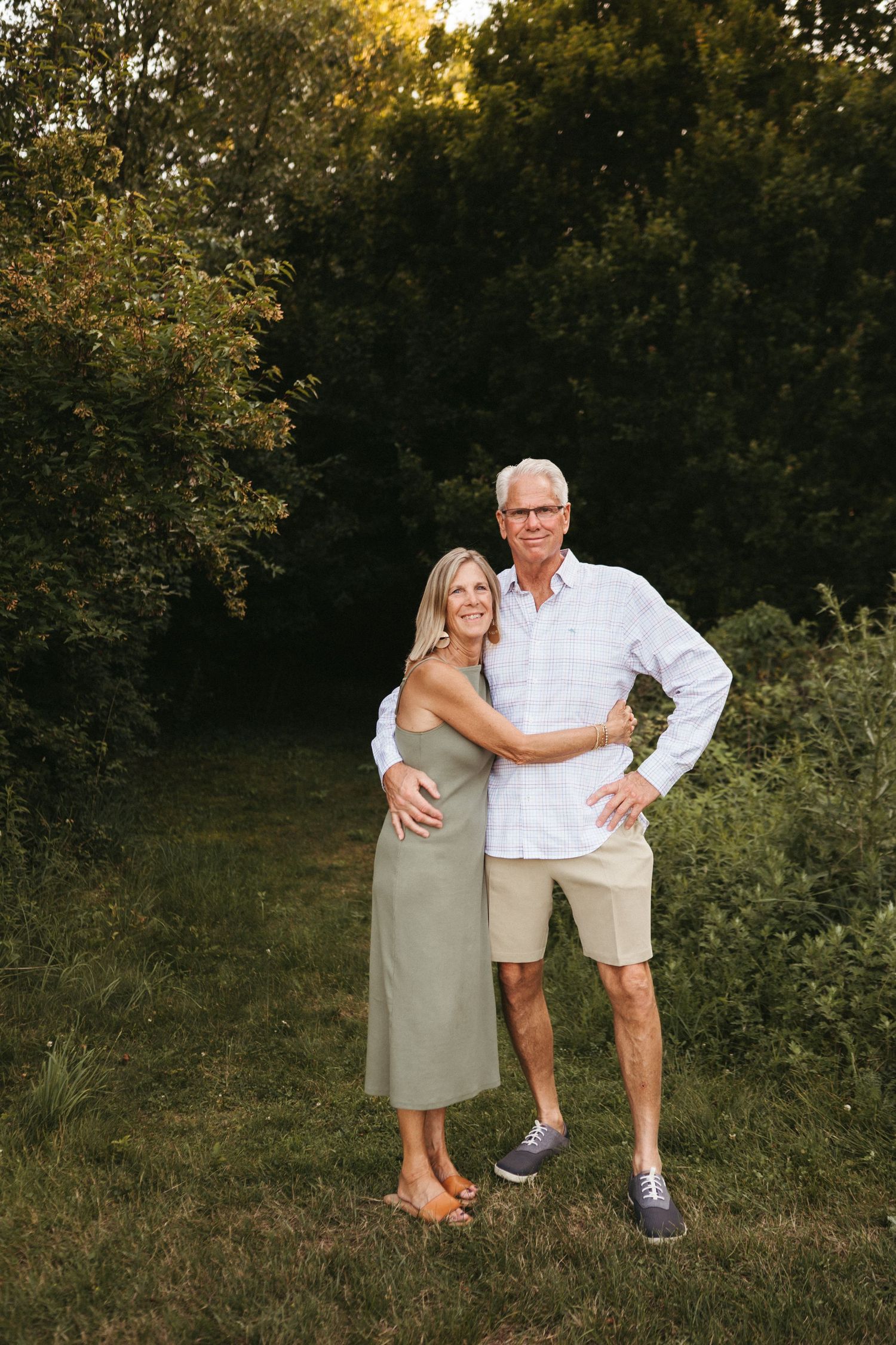 A couple poses together outdoors wearing casual summer attire at sunset.