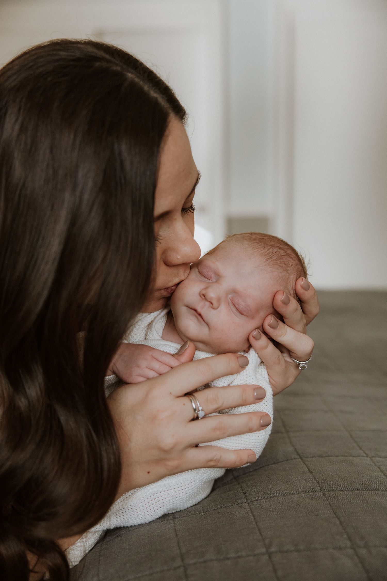 An intimate moment captured as a sleeping newborn receives a gentle kiss in soft lighting.