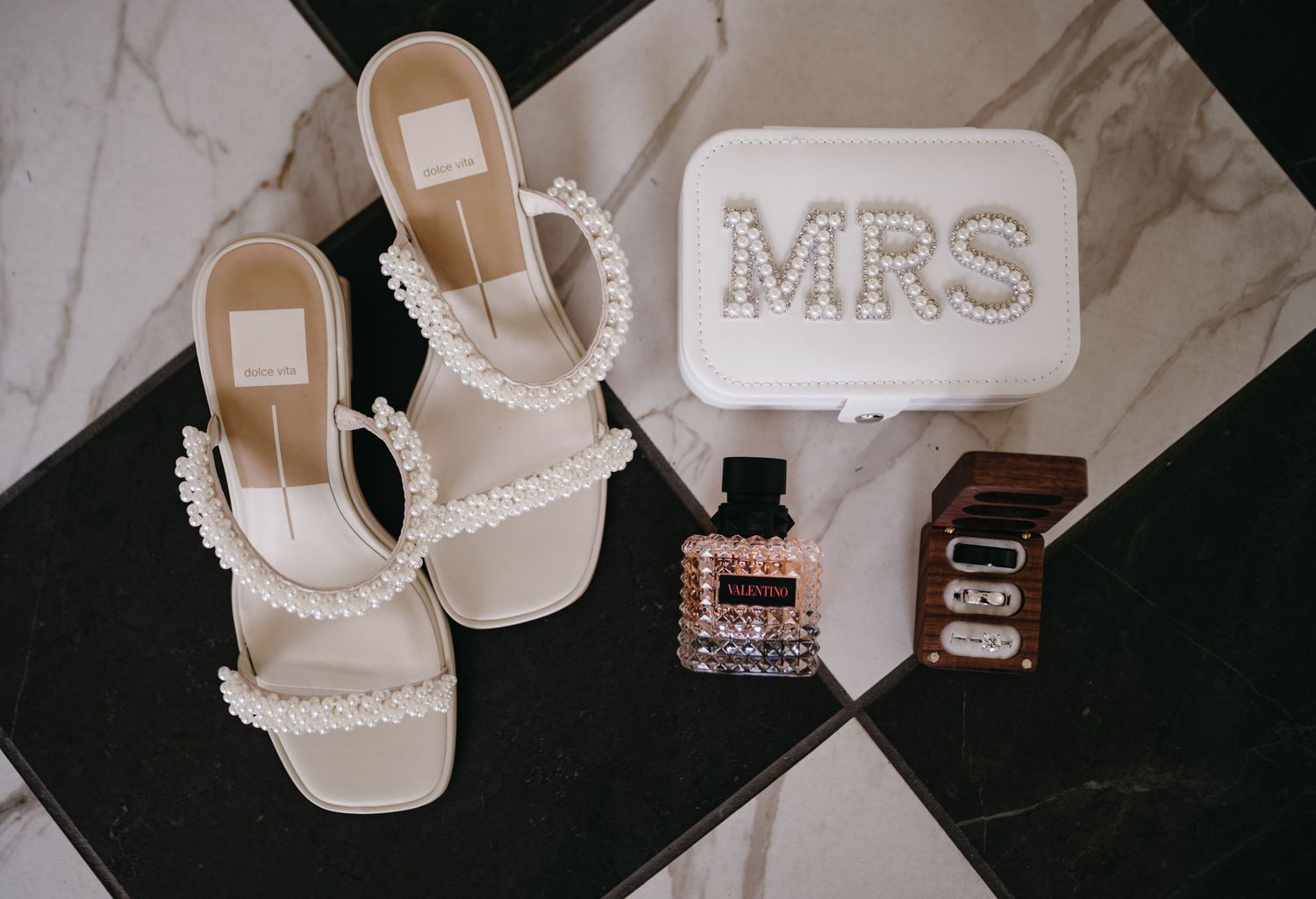 Bridal accessories including pearl-studded sandals and a white 'MRS' clutch on marble tiles.